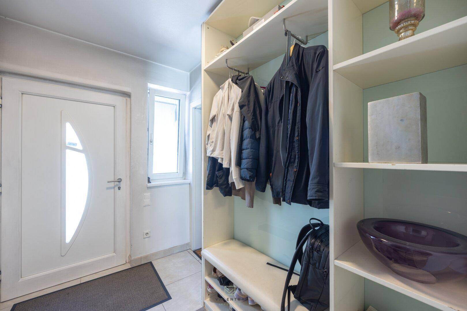 Heller Eingangsbereich mit weißer Tür, Fenster und praktischer Garderobe mit Ablageflächen.