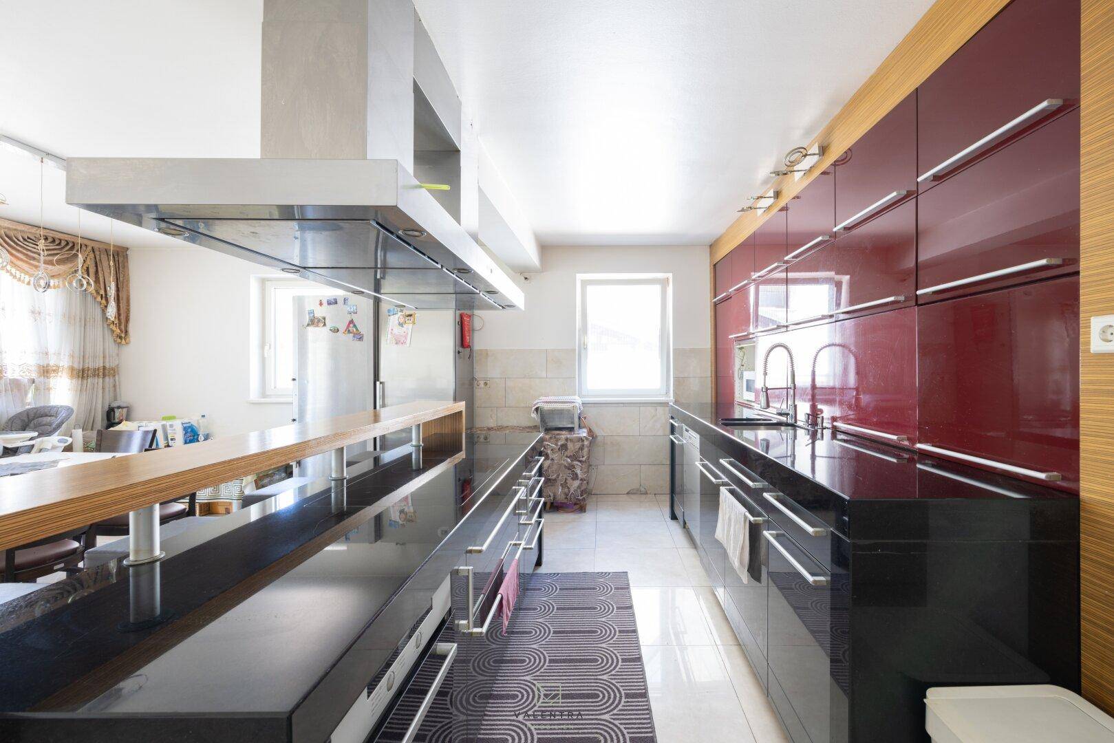 Moderne Küche mit glänzenden roten und schwarzen Schränken, Dunstabzugshaube und Fenster.