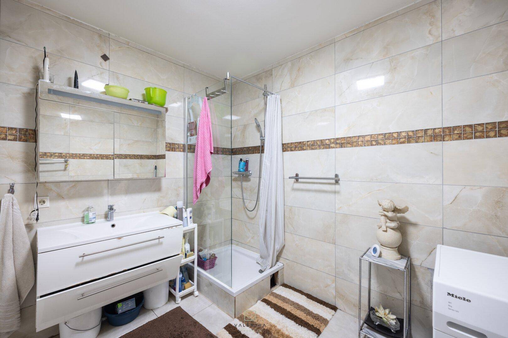 Badezimmer mit Duschkabine, modernem Waschbecken und hellen Fliesen an Wänden und Boden.
