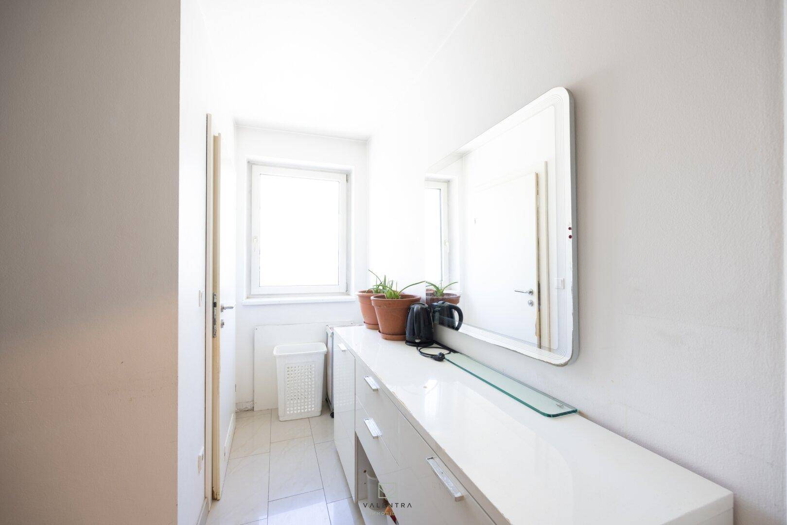 Heller Flur mit weißem Sideboard, großem Spiegel und Fenster für natürliches Licht.
