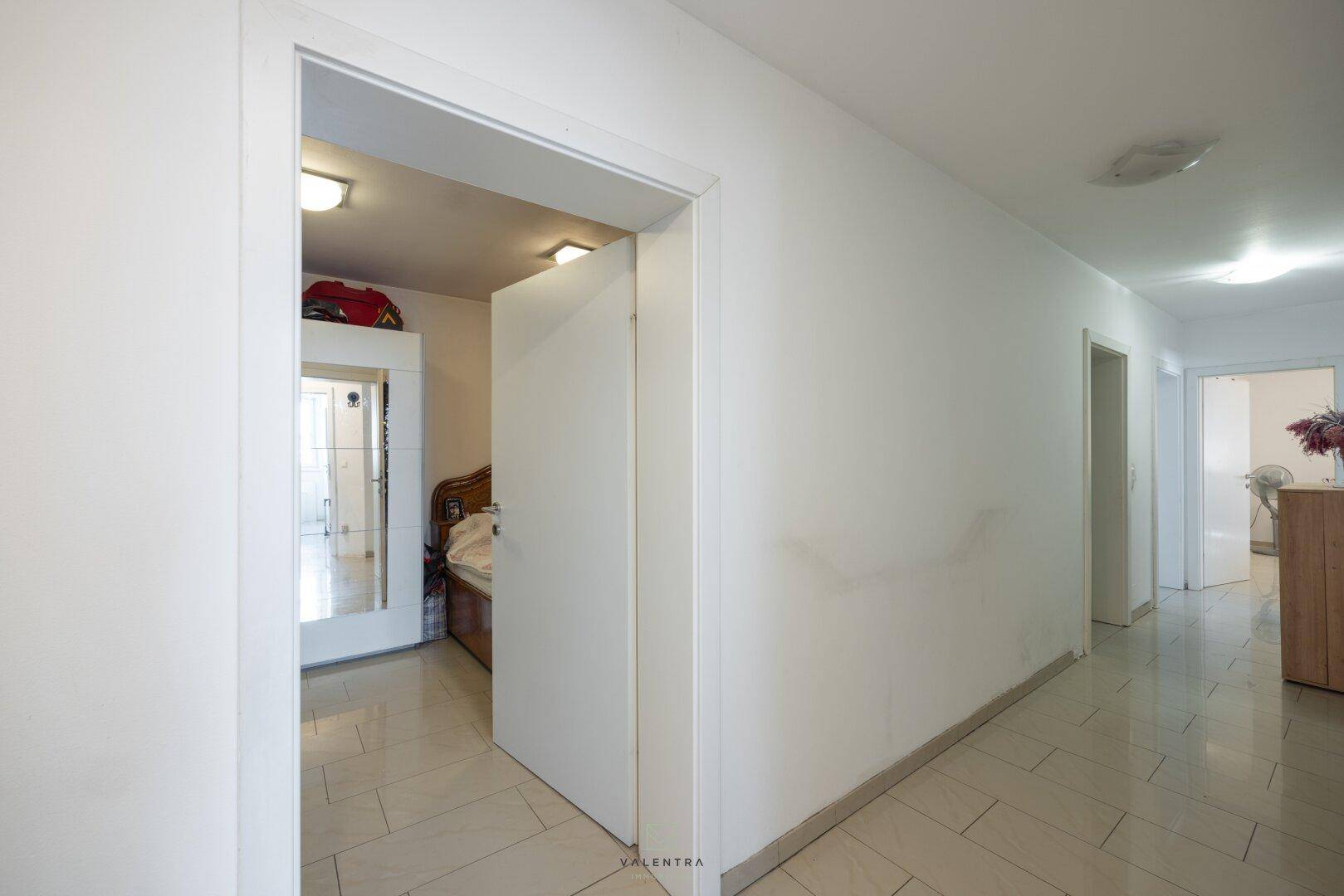 Langer, heller Flur mit Fliesenboden, der zu einem Schlafzimmer und weiteren Räumen führt.