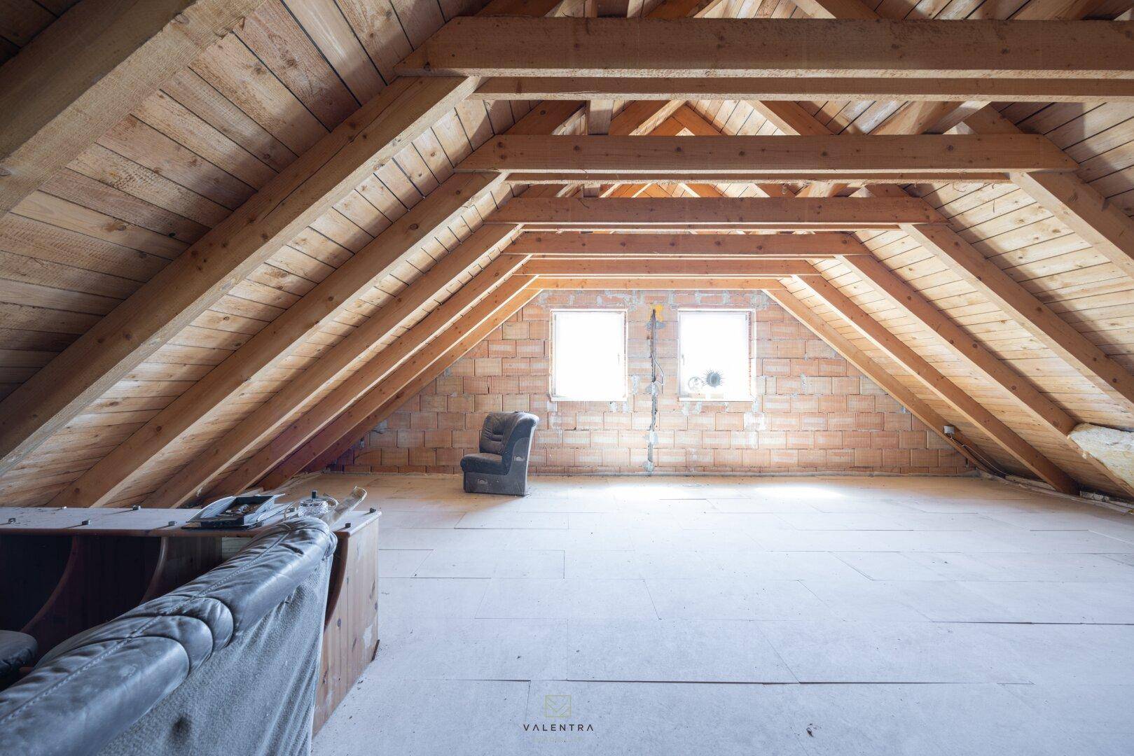 Geräumiger Dachboden mit sichtbaren Holzbalken und zwei Fenstern, bereit für den Ausbau.