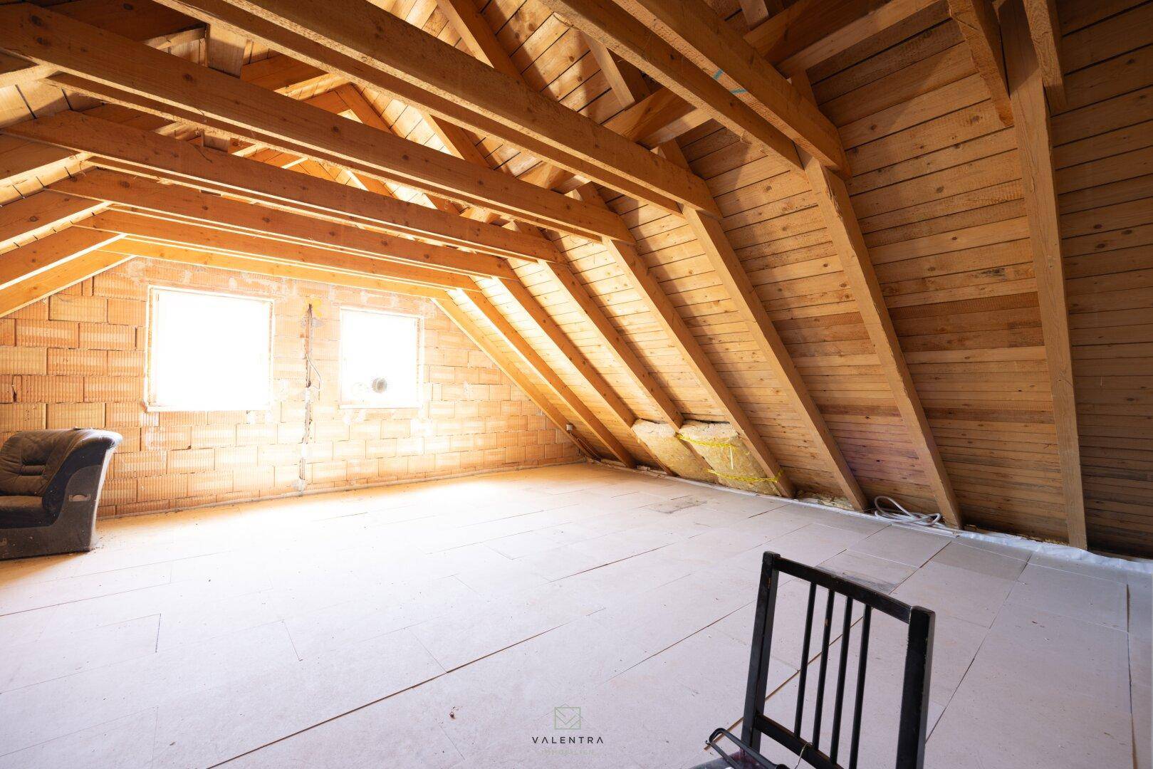 Heller Dachboden mit freiliegenden Holzbalken und Fenstern, bietet Potenzial für zusätzlichen Wohnraum.