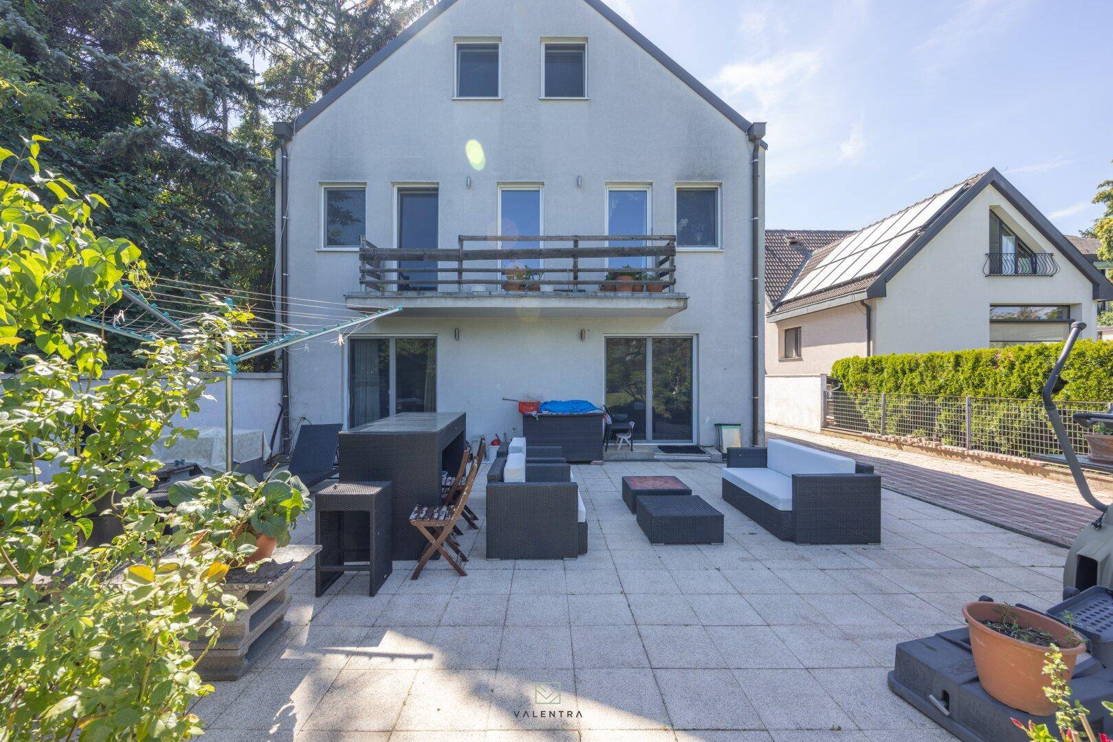 Geräumige Terrasse mit modernen Gartenmöbeln und Blick auf die Rückseite des Hauses mit Balkonen.