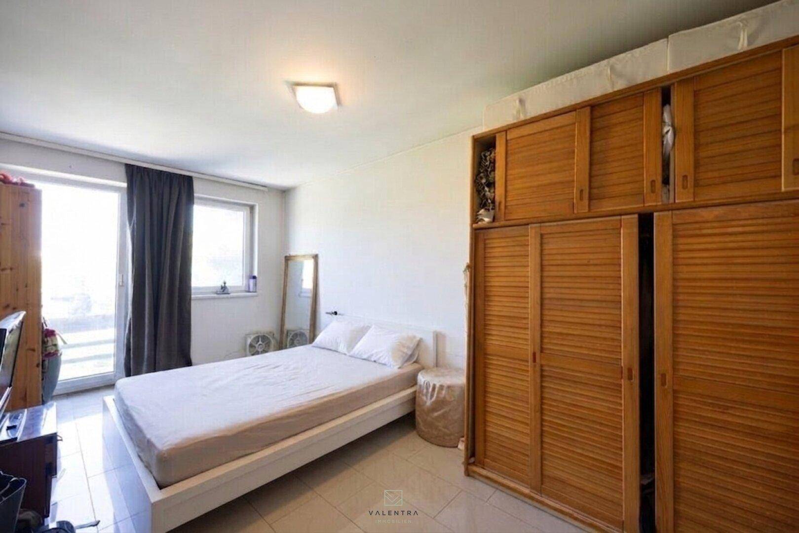 Helles Schlafzimmer mit Doppelbett, großem Holzschrank und Fenster für viel Tageslicht.