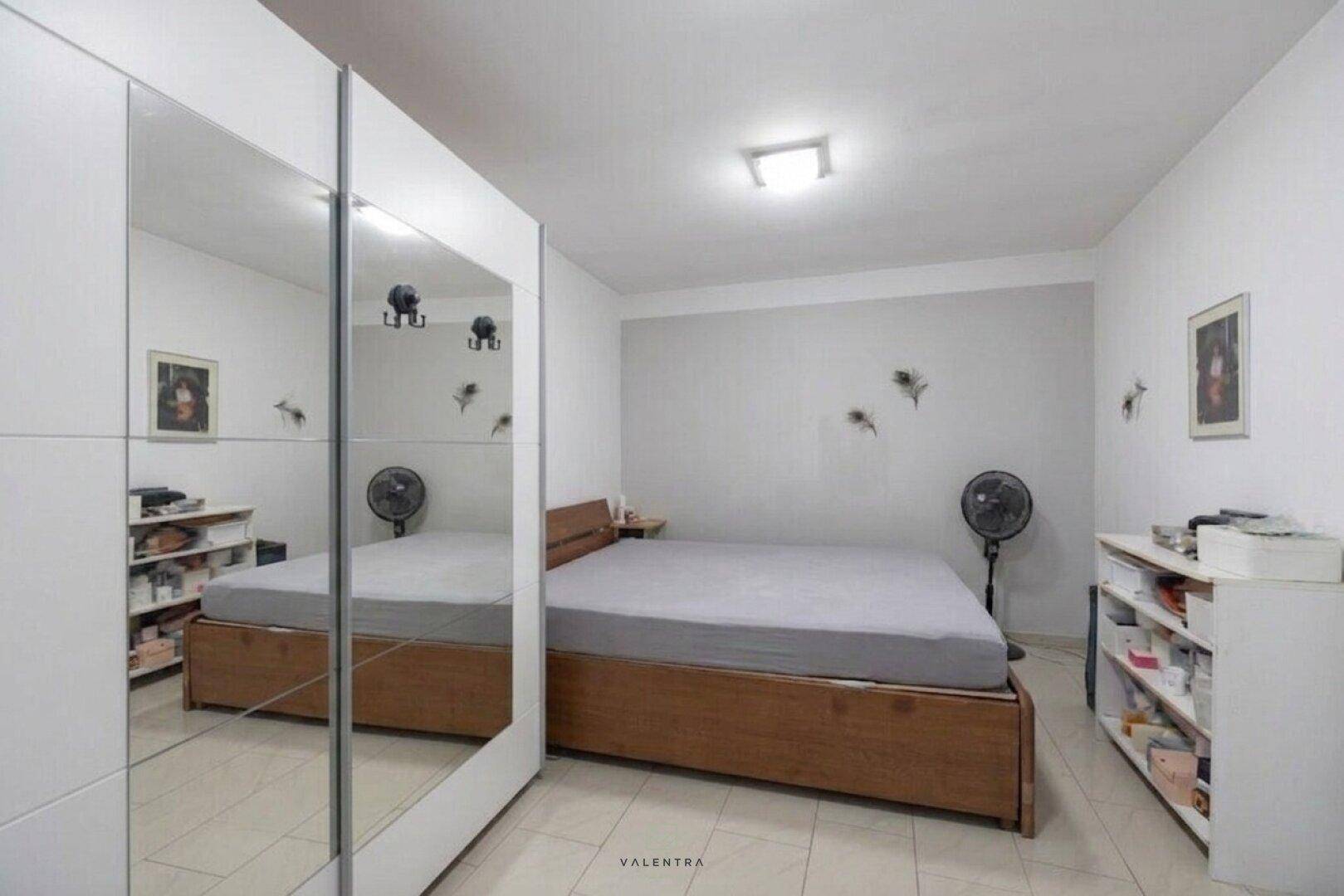 Schlafzimmer mit Holzbett, großem Spiegelschrank und Fliesenboden, hell und funktional eingerichtet.