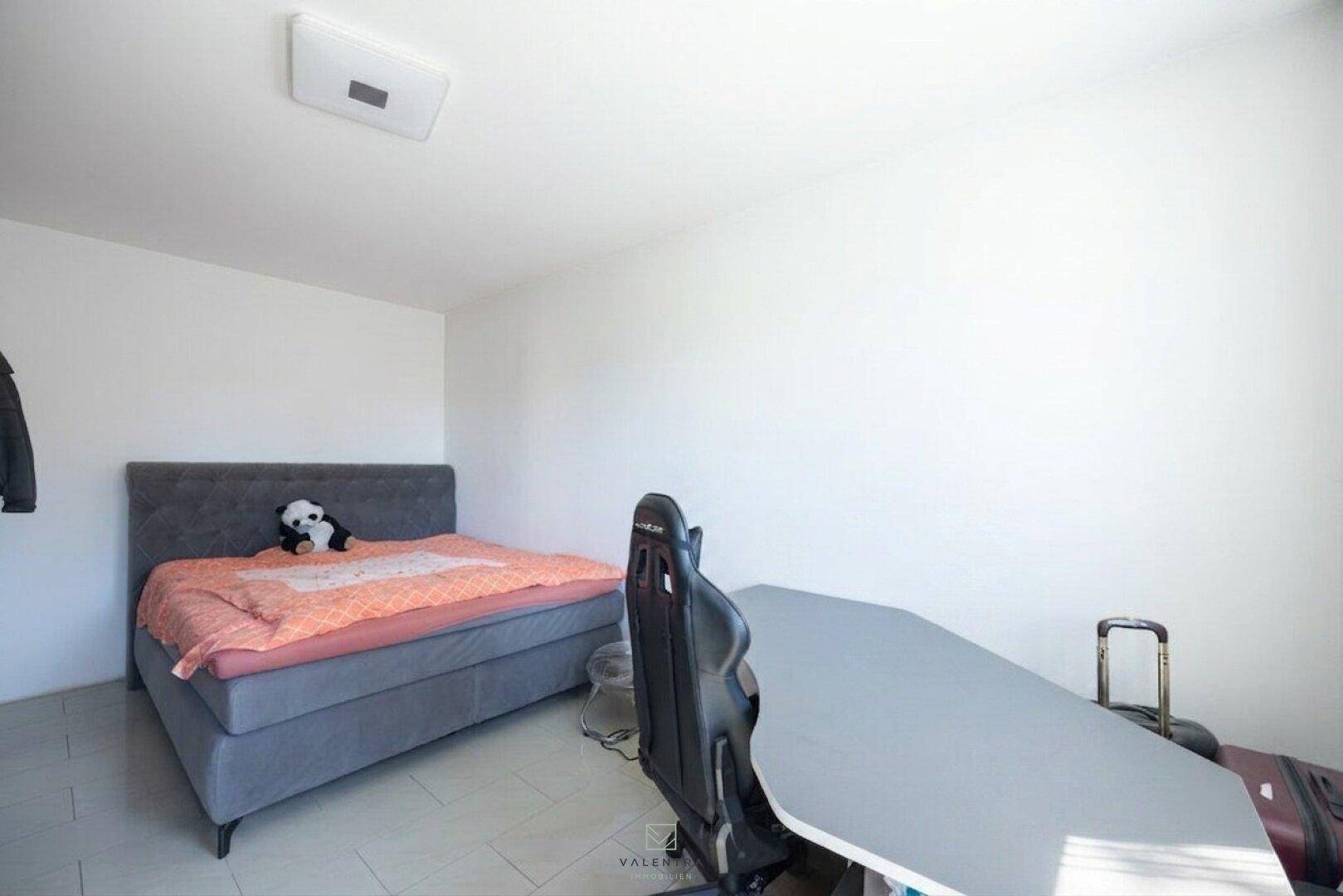 Schlafzimmer mit Bett und Schreibtisch, ideal als Jugendzimmer oder Arbeitsbereich, mit hellem Fliesenboden.