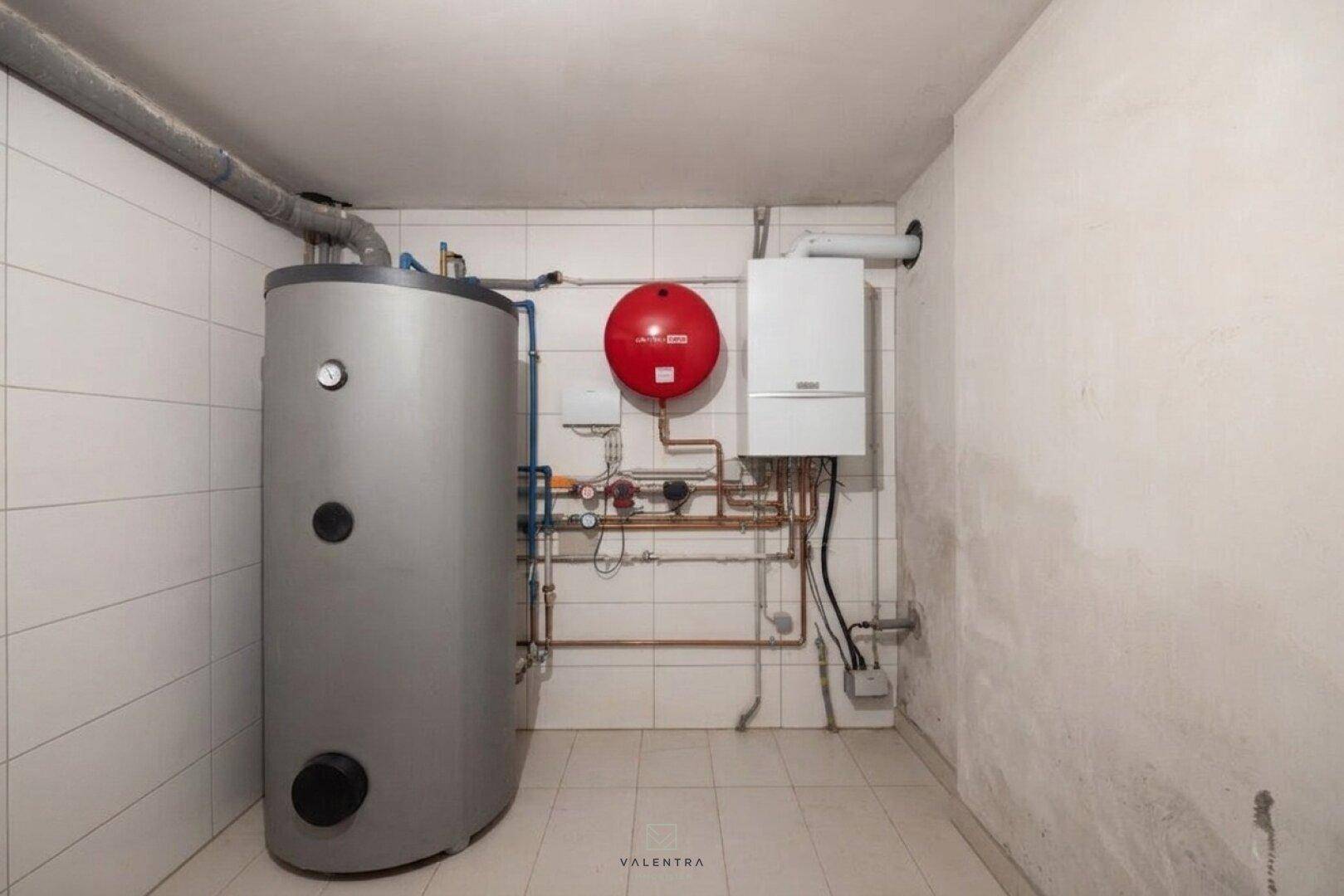 Technikraum im Keller mit Warmwasserspeicher und Heizungsanlage, auf gefliestem Boden.