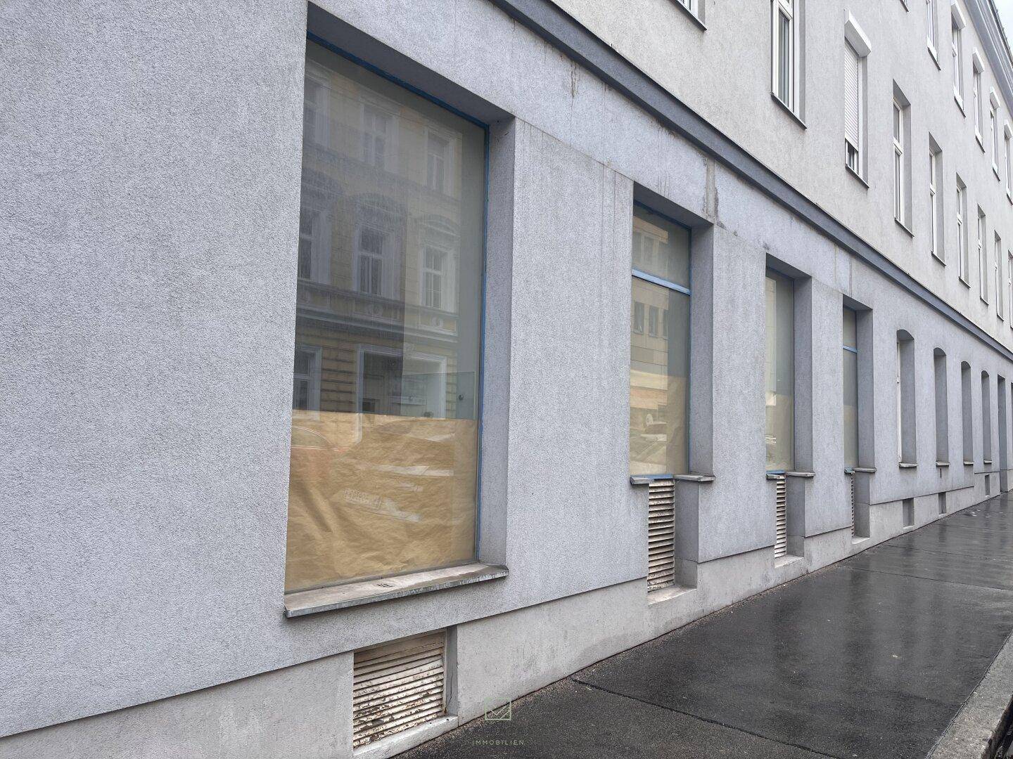 Lange Fassade eines Gebäudes mit mehreren großen Fenstern, die mit Papier abgedeckt sind, an einer Straße.