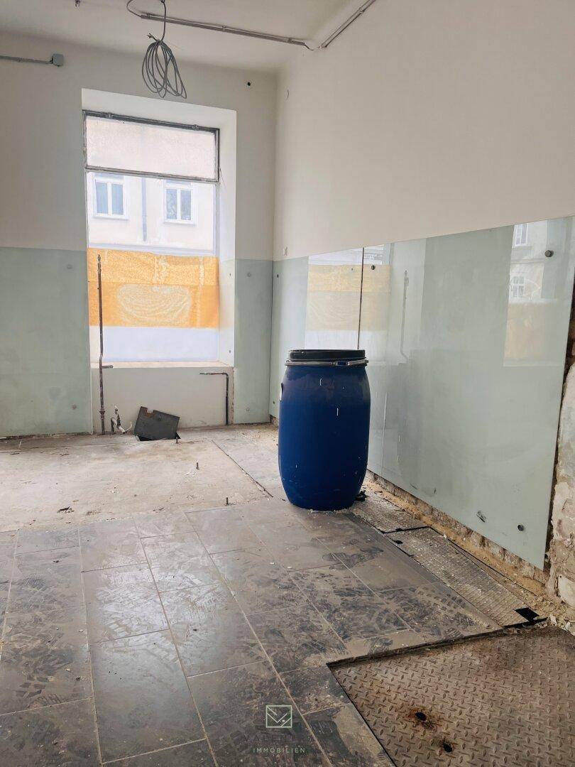 Innenraum mit großen Fenstern, die mit Papier abgedeckt sind, und einem blauen Fass in der Mitte des Raumes.
