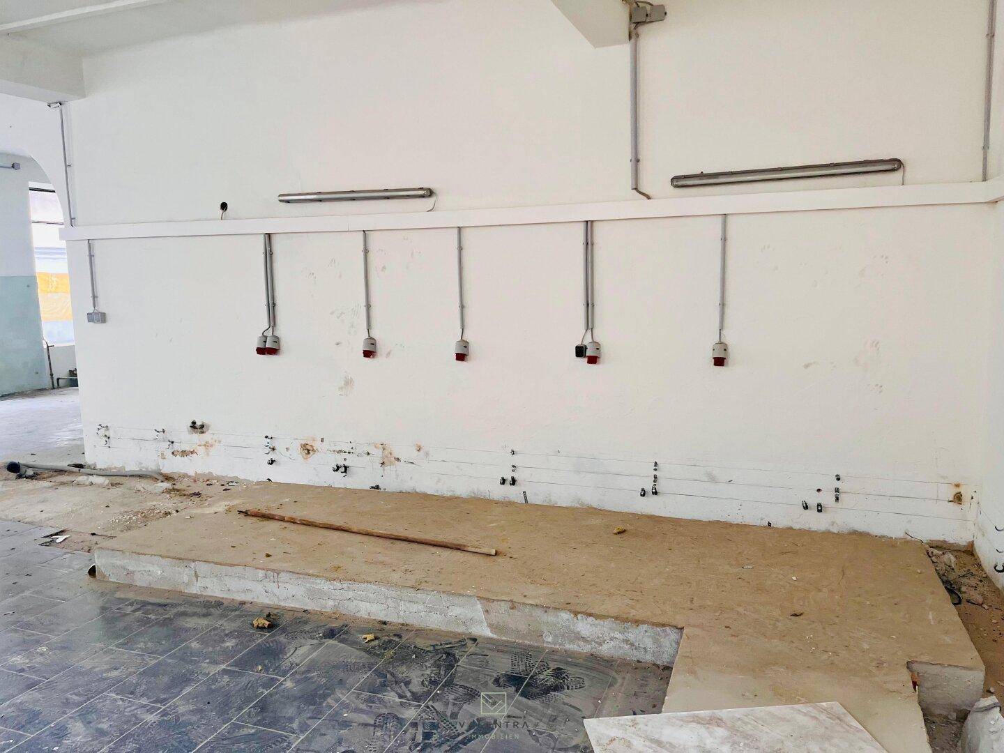 Wandbereich mit sichtbaren elektrischen Installationen und einer erhöhten Plattform im Vordergrund des Raumes.