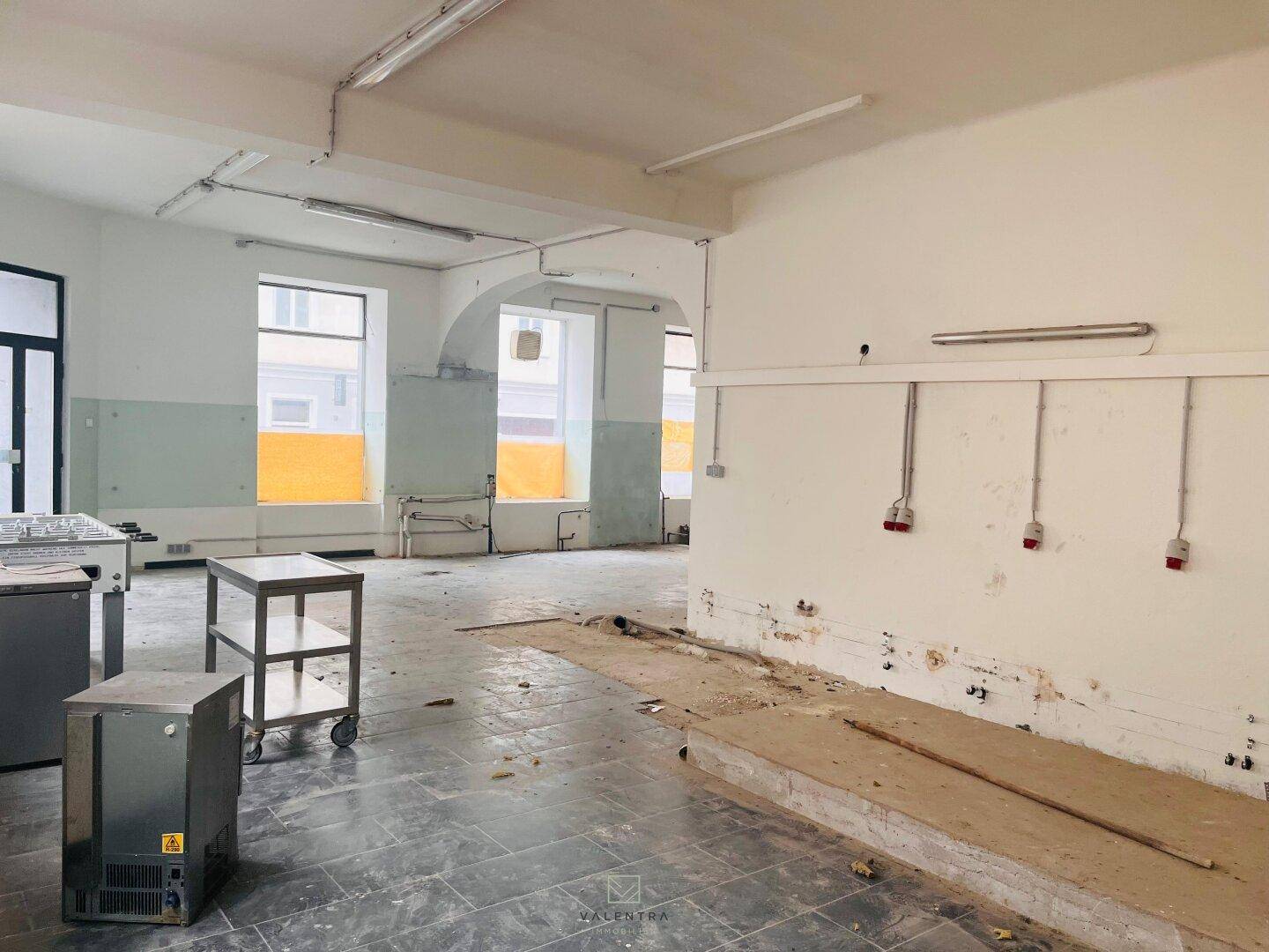 Großer Innenraum mit Fenstern, einer erhöhten Plattform und sichtbaren elektrischen Anschlüssen an der Wand.