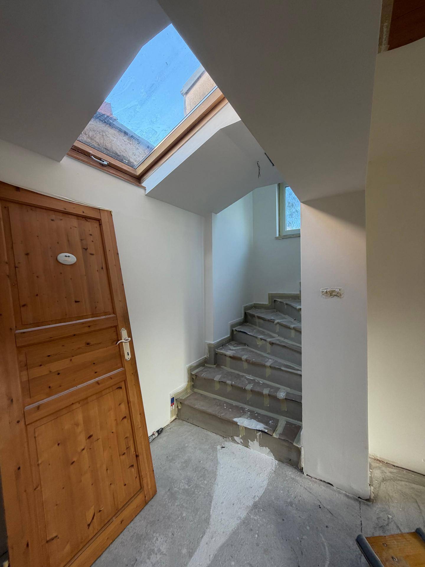 Treppenhaus im Umbau mit Oberlichtfenster und Holztür, viel natürliches Licht.