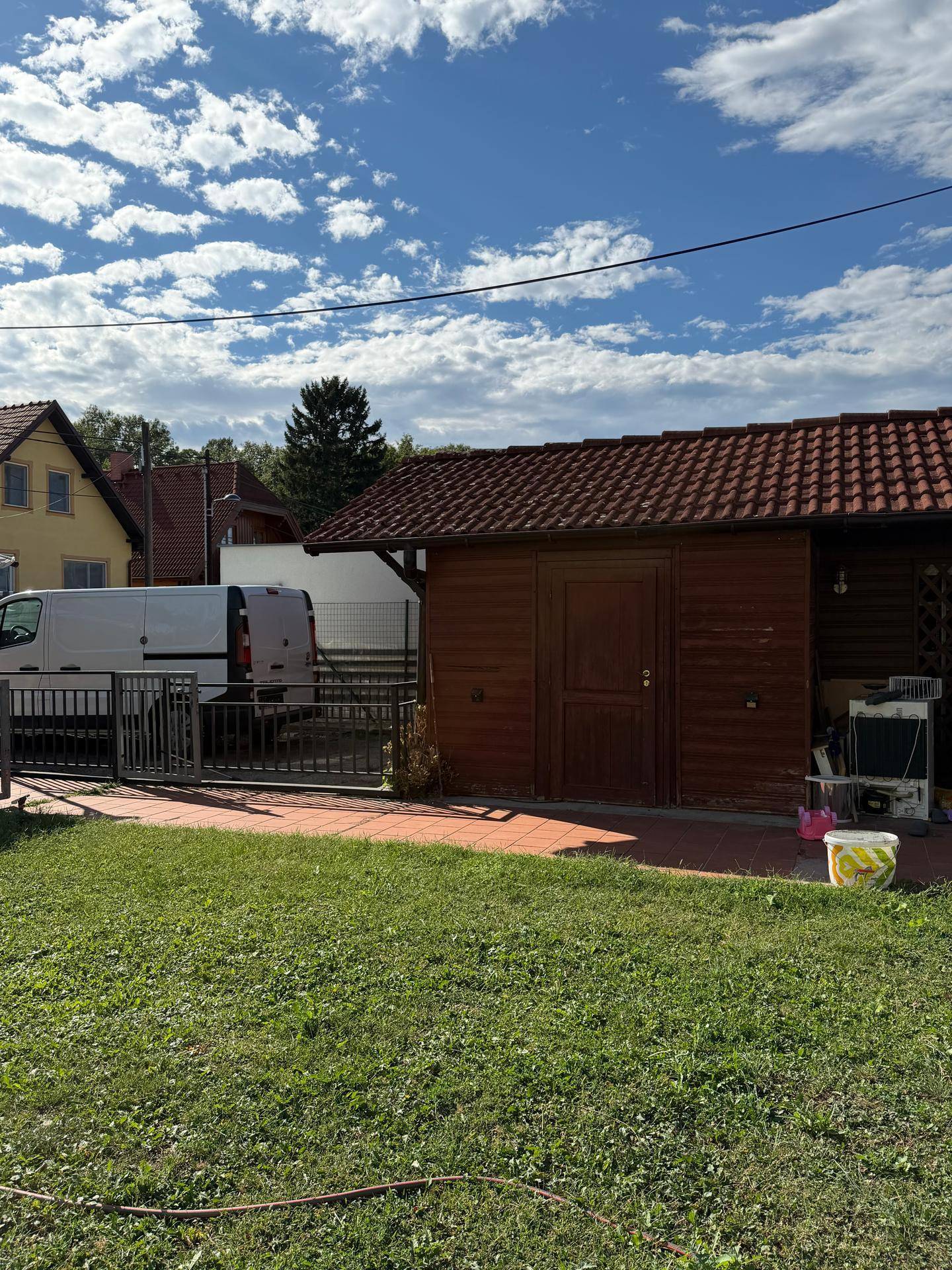 Kleiner Holzschuppen mit Ziegeldach neben einem geparkten Lieferwagen und Rasenfläche.