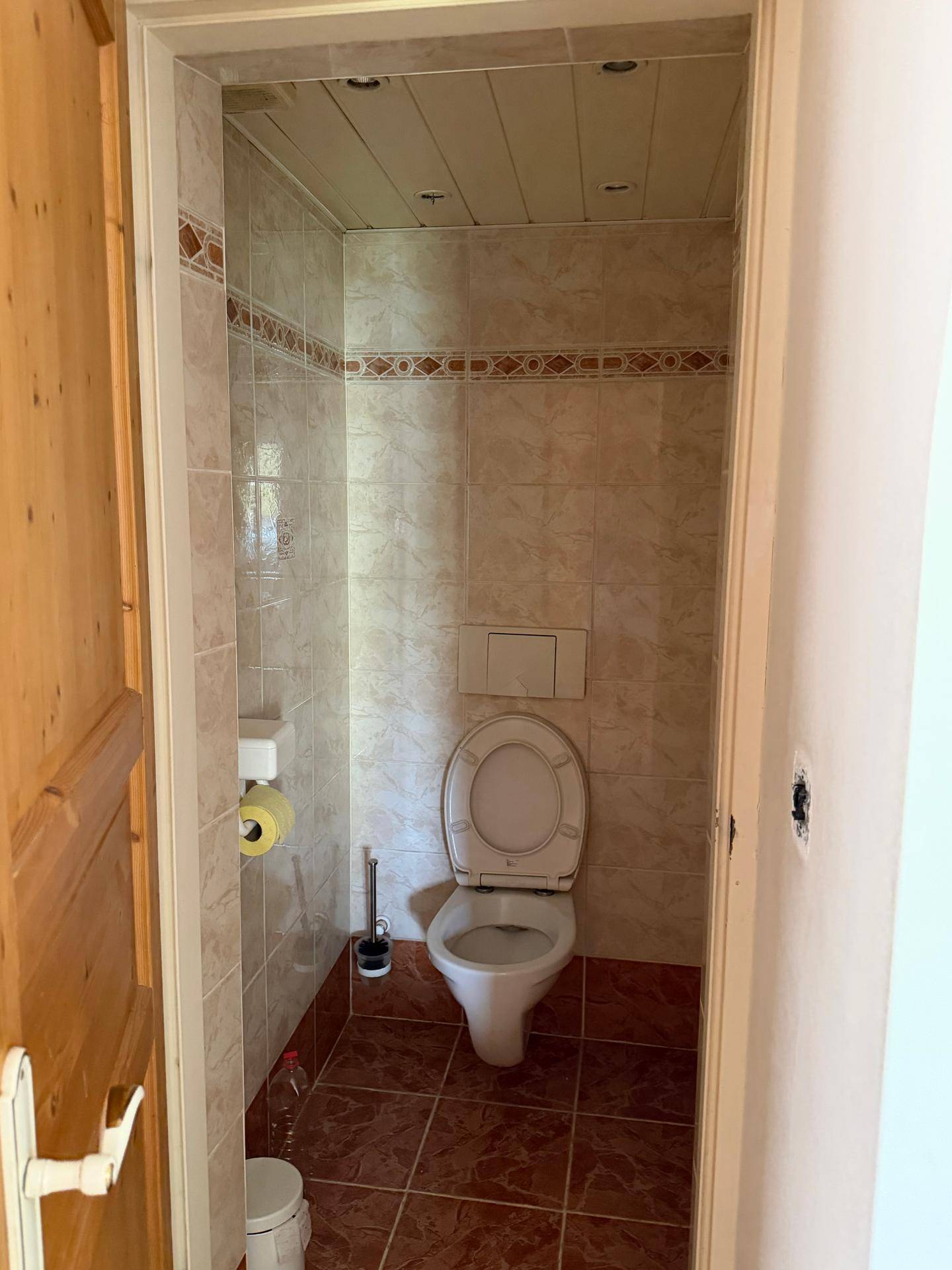 Kleines WC mit braunen Bodenfliesen und hellen Wandfliesen, funktional und sauber.