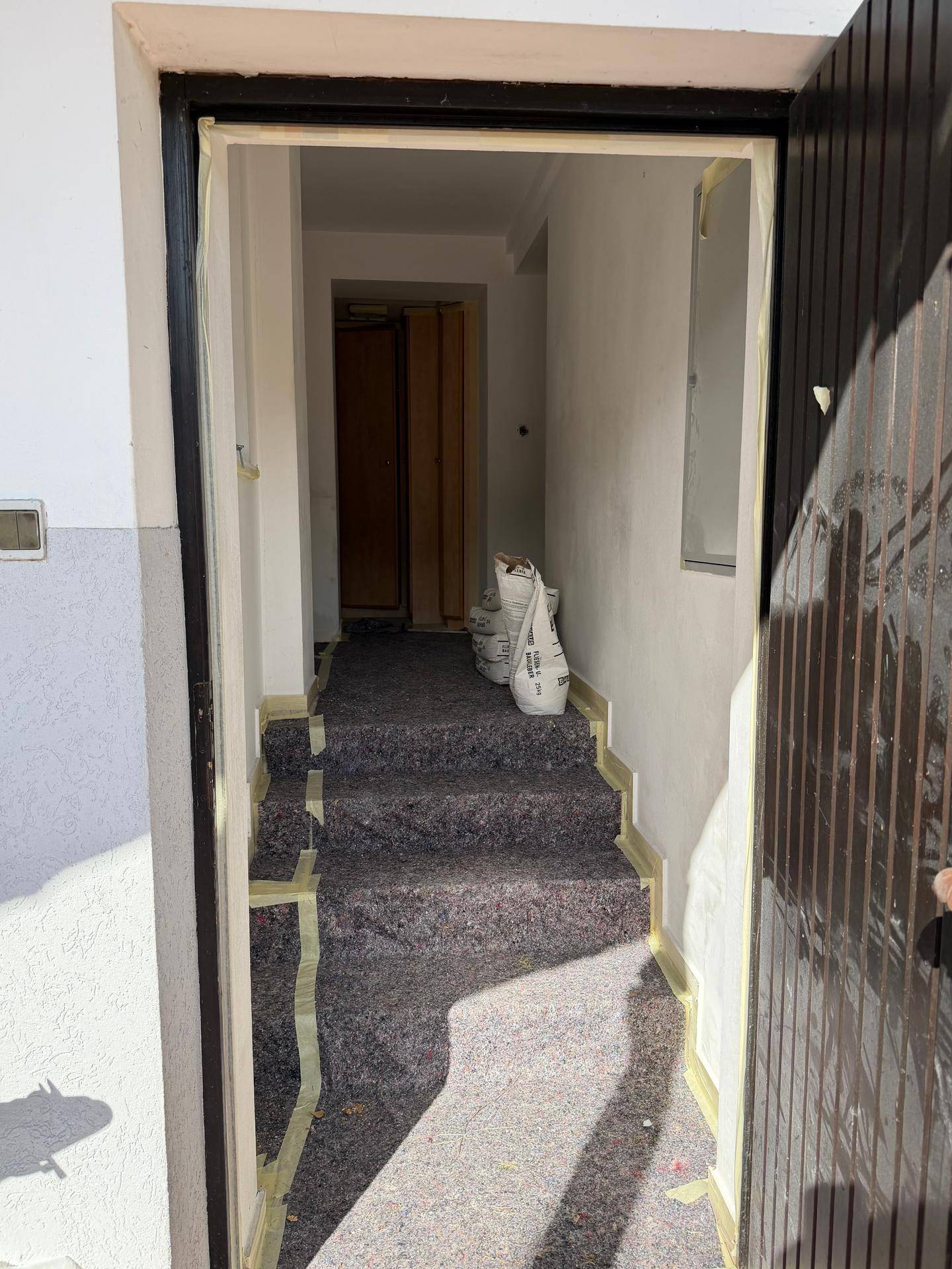 Eingangsbereich im Umbau mit abgedeckten Stufen und Blick in den Flur, bereit zur Renovierung.