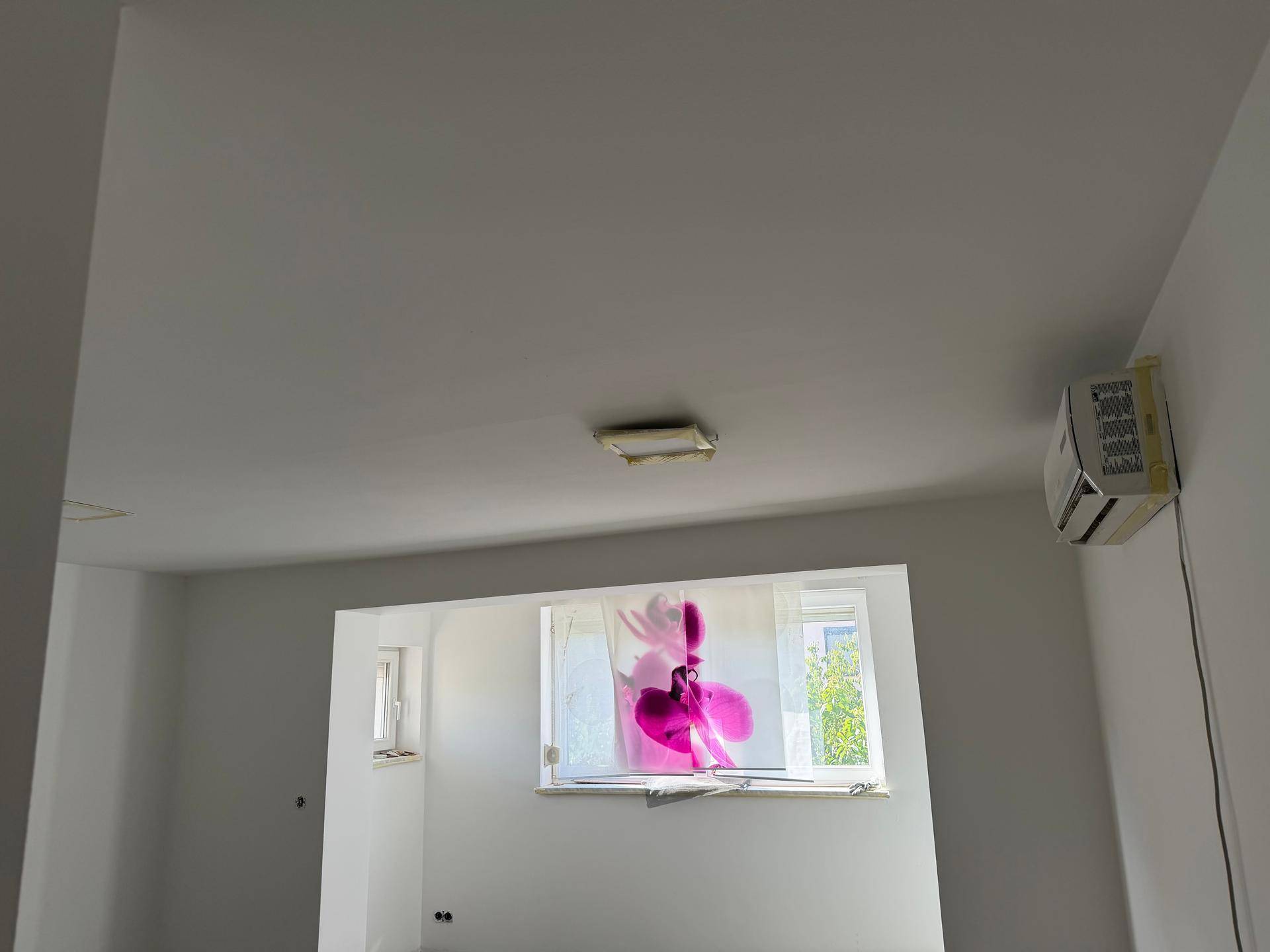 Raum im Umbau mit Klimaanlage und einem Fenster mit Vorhang, hell und funktional.