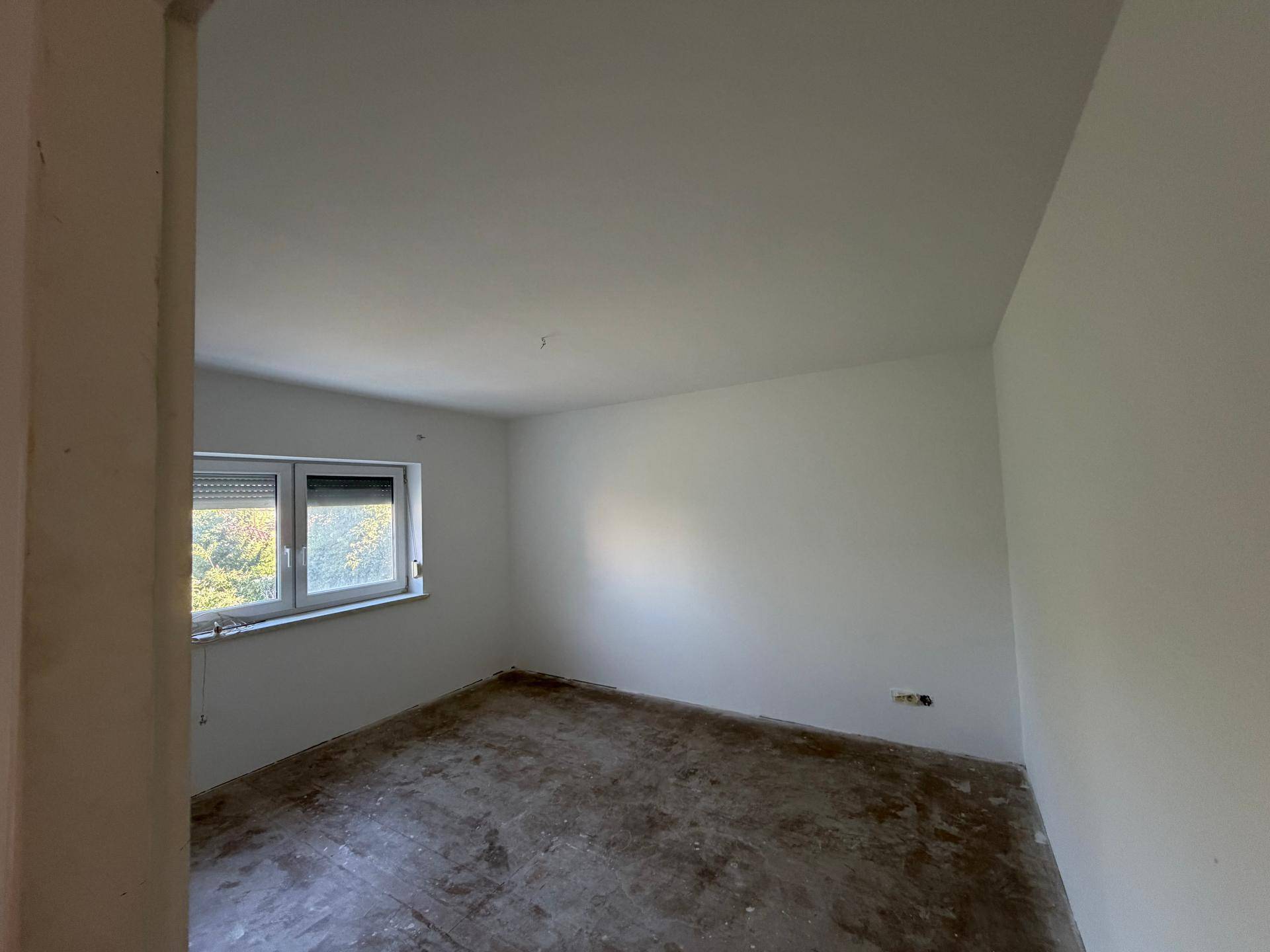 Schlafzimmer im Umbau mit einem Fenster und Blick ins Grüne, bereit zur Fertigstellung.