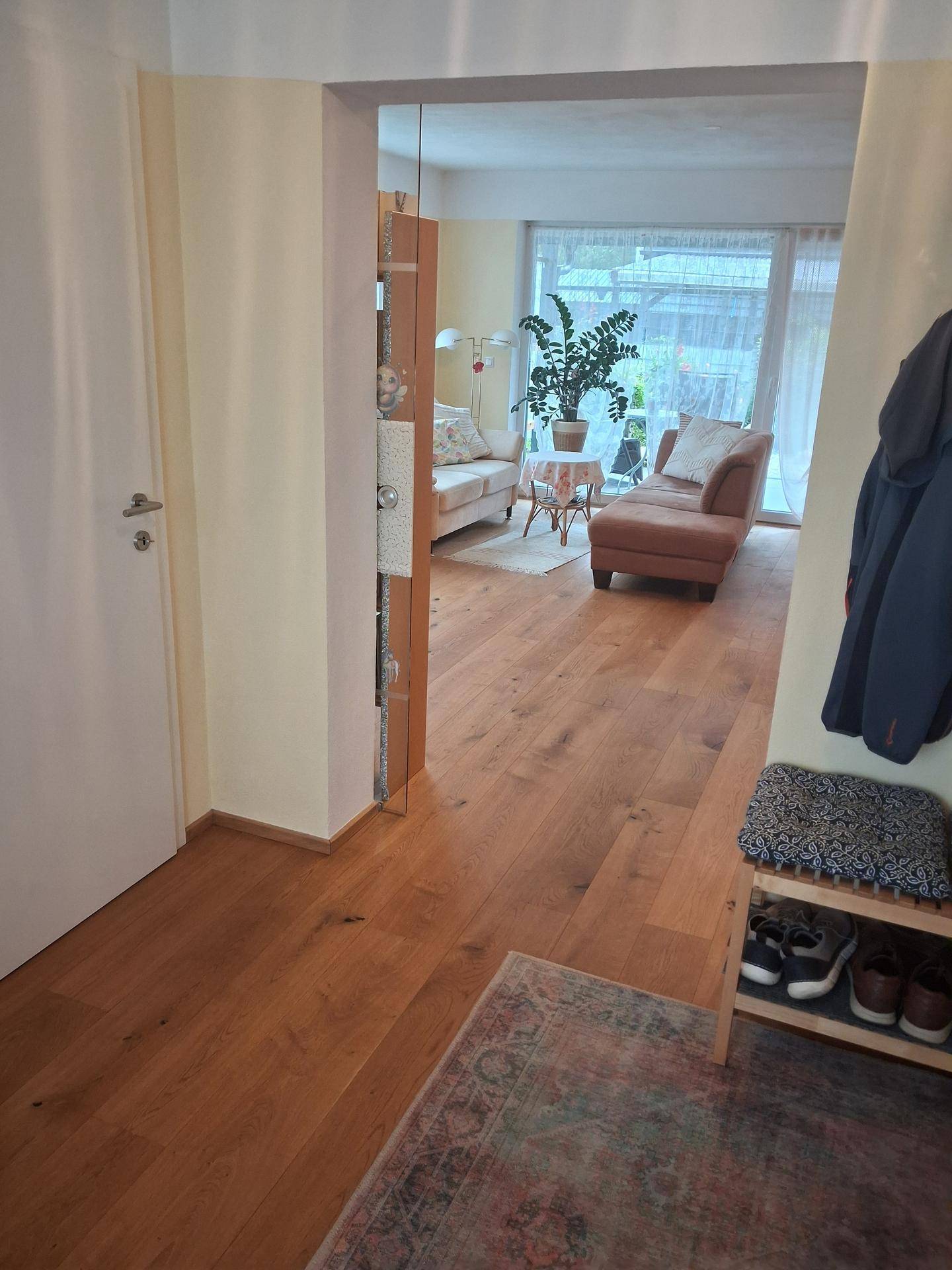 Heller Eingangsbereich mit Holzboden, der in ein gemütliches Wohnzimmer führt.