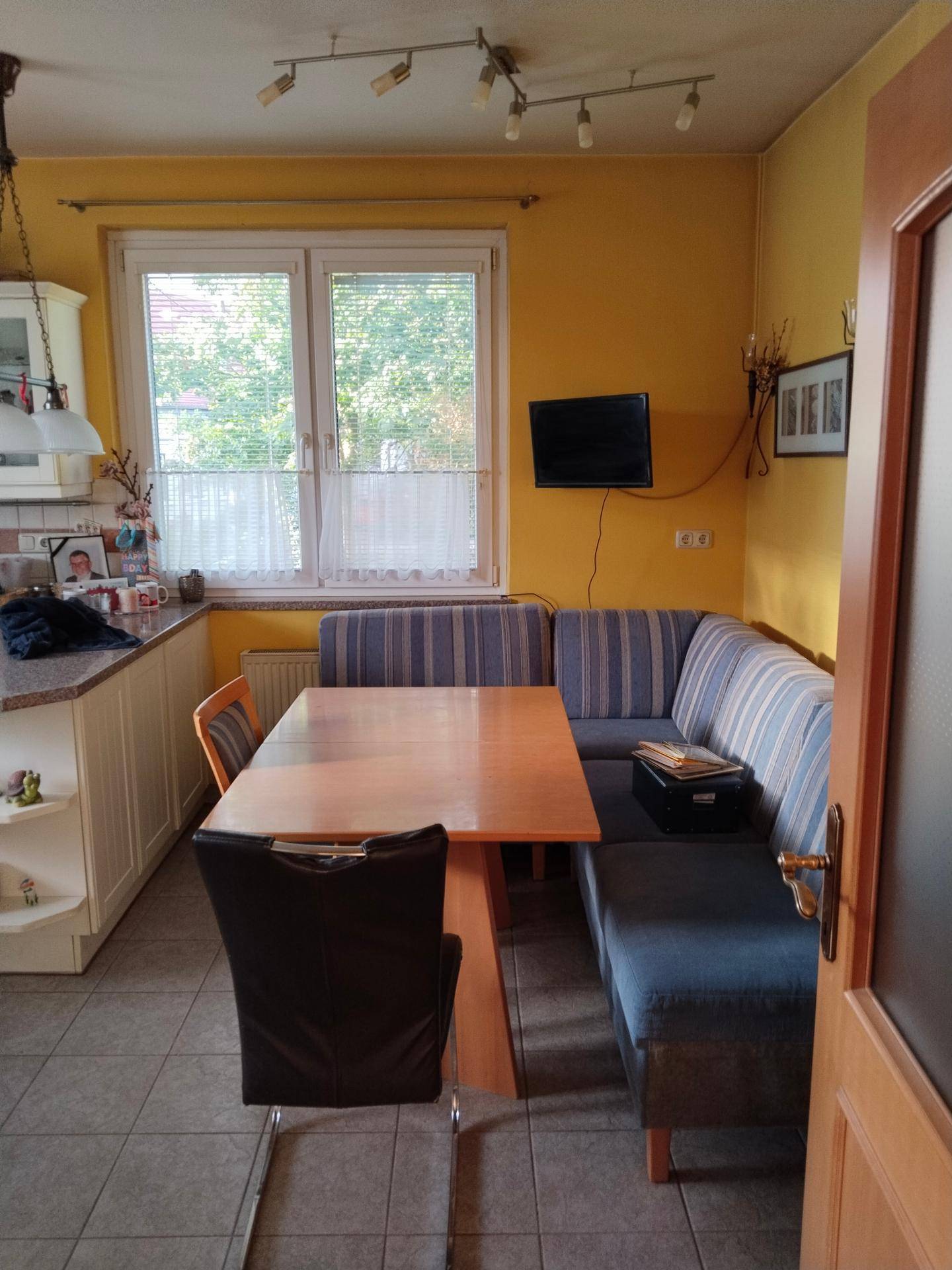 Gemütliche Küche mit gelben Wänden, integriertem Essbereich und Fenster mit Blick ins Grüne.