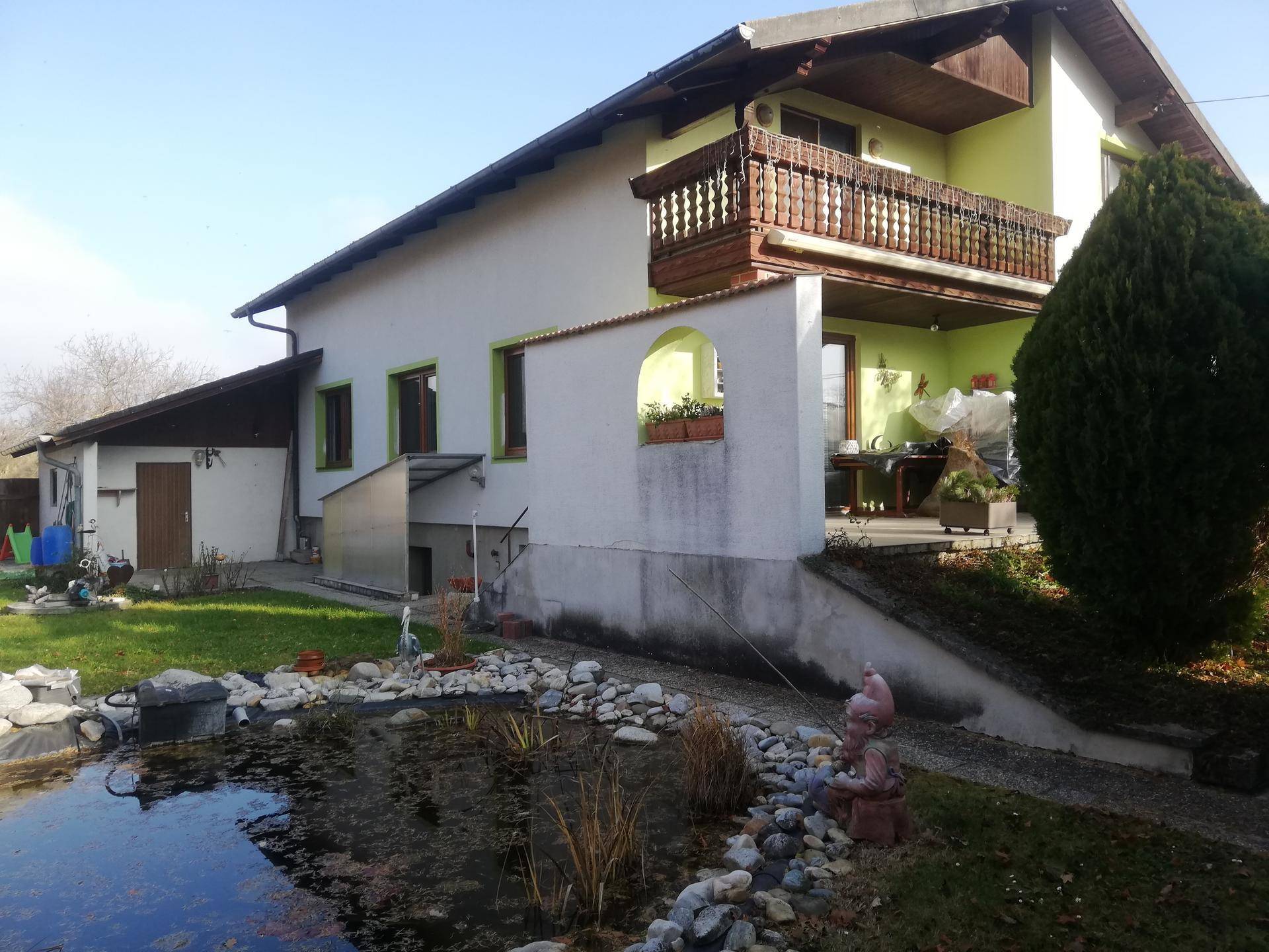 Rückansicht des Hauses mit Teich im Garten und überdachter Terrasse im Erdgeschoss.