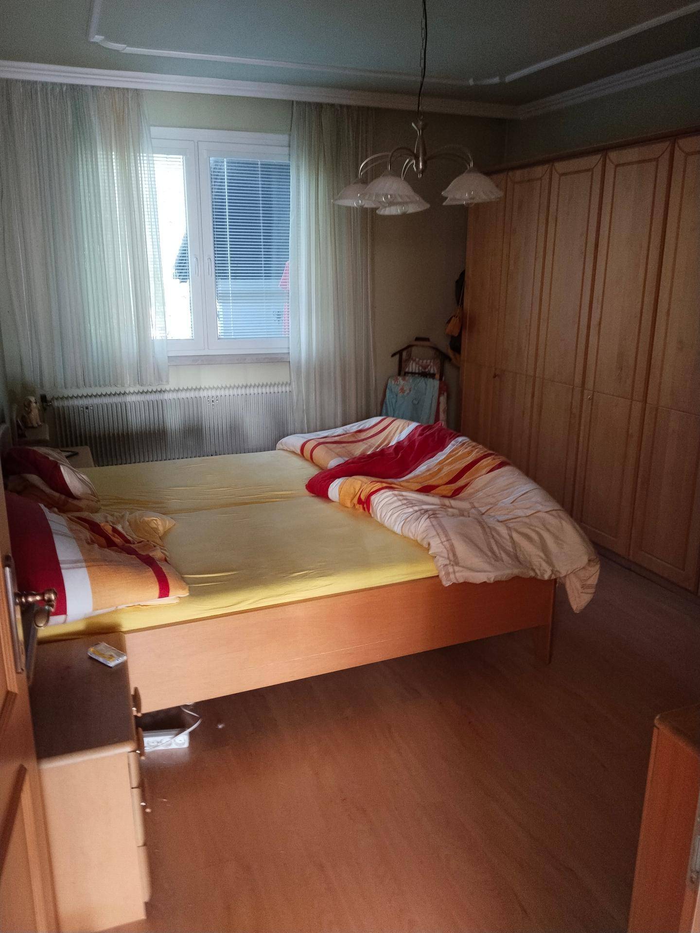 Schlafzimmer mit Holzboden, Doppelbett und großem Kleiderschrank aus hellem Holz, gut beleuchtet.