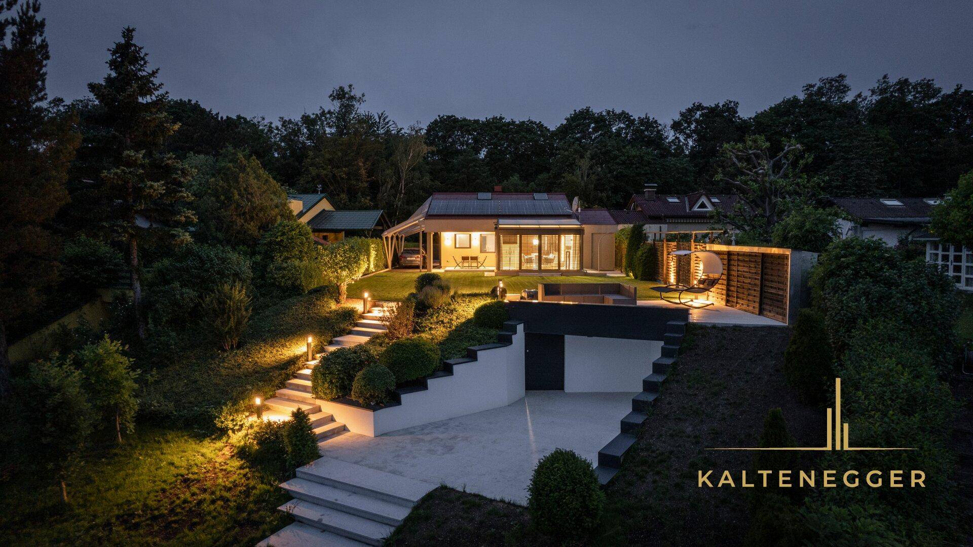 Moderne Villa bei Nacht mit beleuchtetem Garten, Pool und Zufahrt.