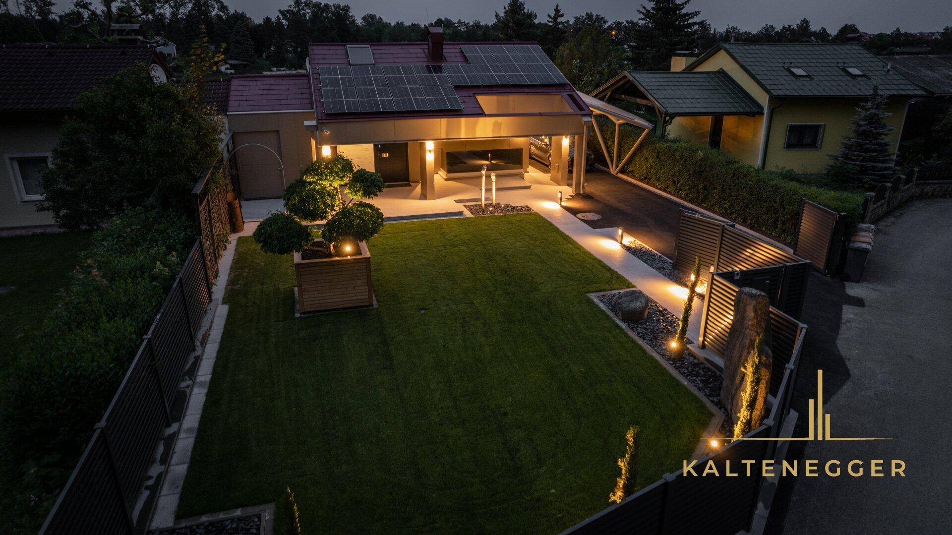 Vorderansicht der modernen Villa bei Nacht mit gepflegtem Rasen und Beleuchtung.