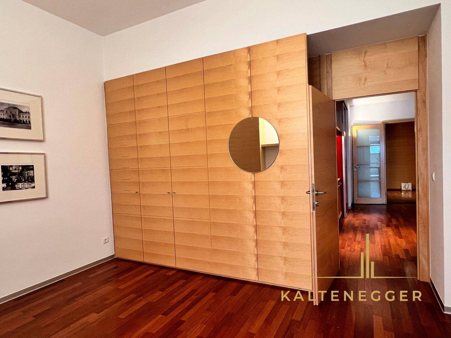 Zimmer mit Holzboden und einer großen, integrierten Holzschrankwand mit rundem Spiegel.