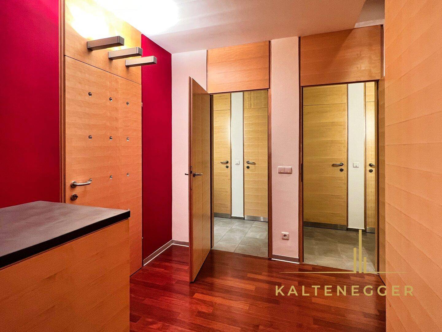 Heller Flur mit Holzboden, roten Akzentwänden und mehreren Holztüren, die zu weiteren Räumen führen.