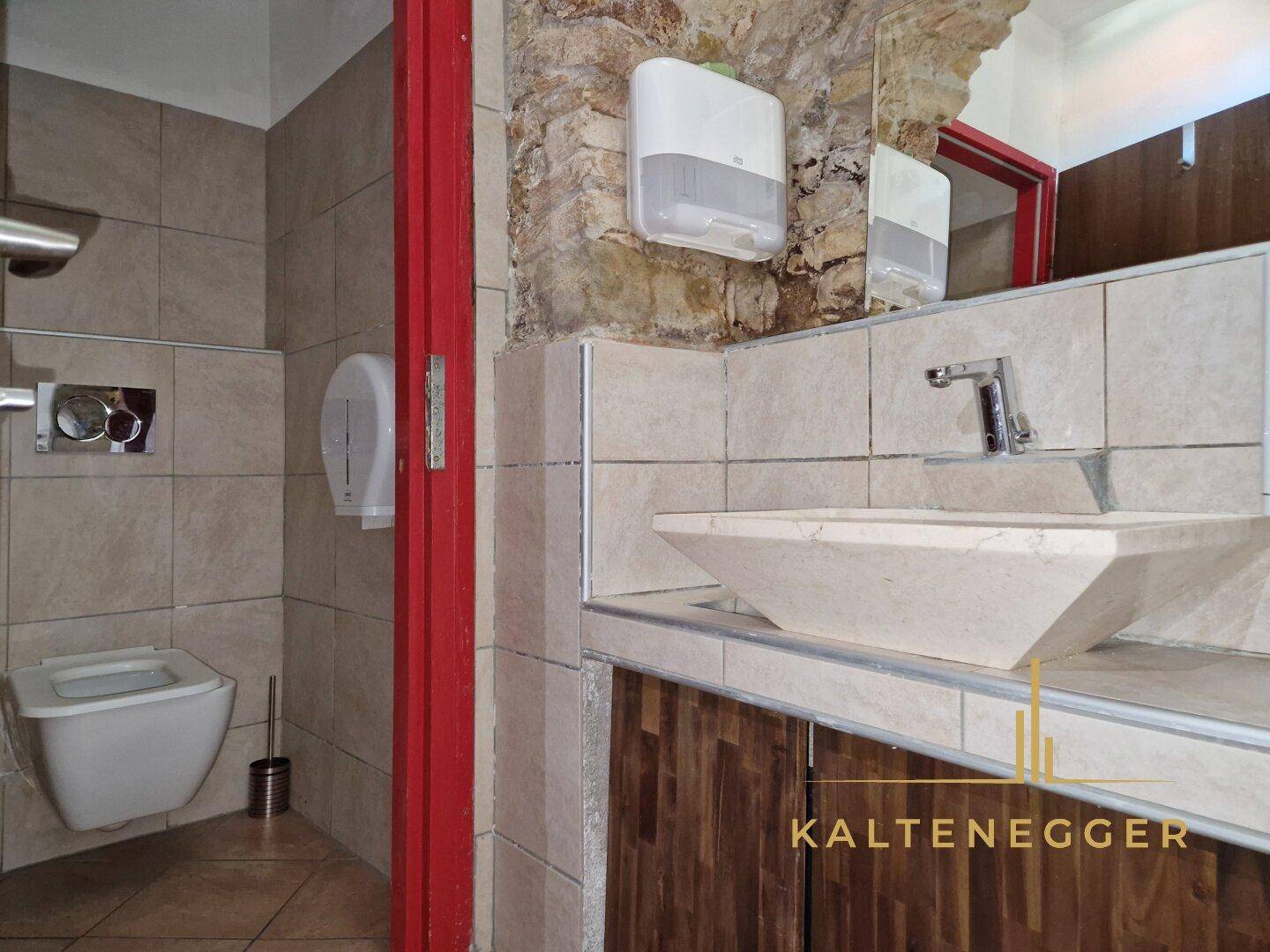 Modernes Badezimmer mit gefliesten Wänden, freiliegender Steinwand und einem stilvollen Aufsatzwaschbecken.