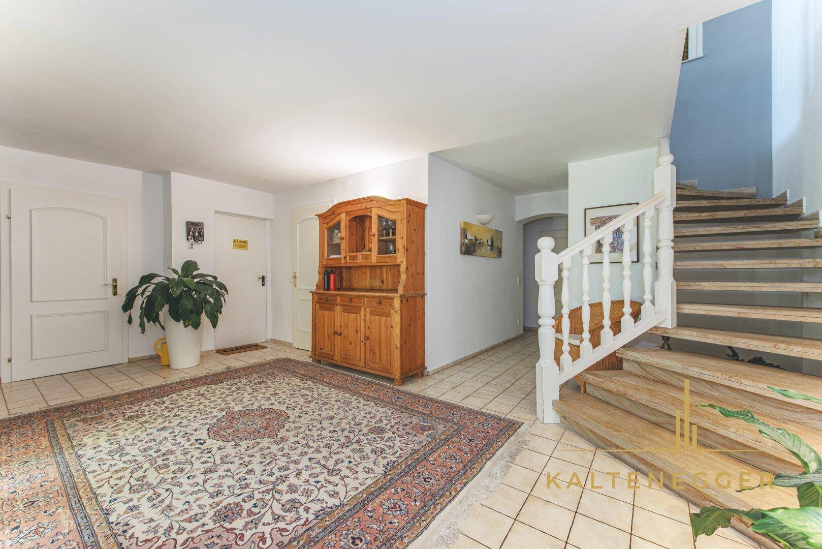 Heller Eingangsbereich mit Holztreppe, Fliesenboden und traditionellem Holzschrank.