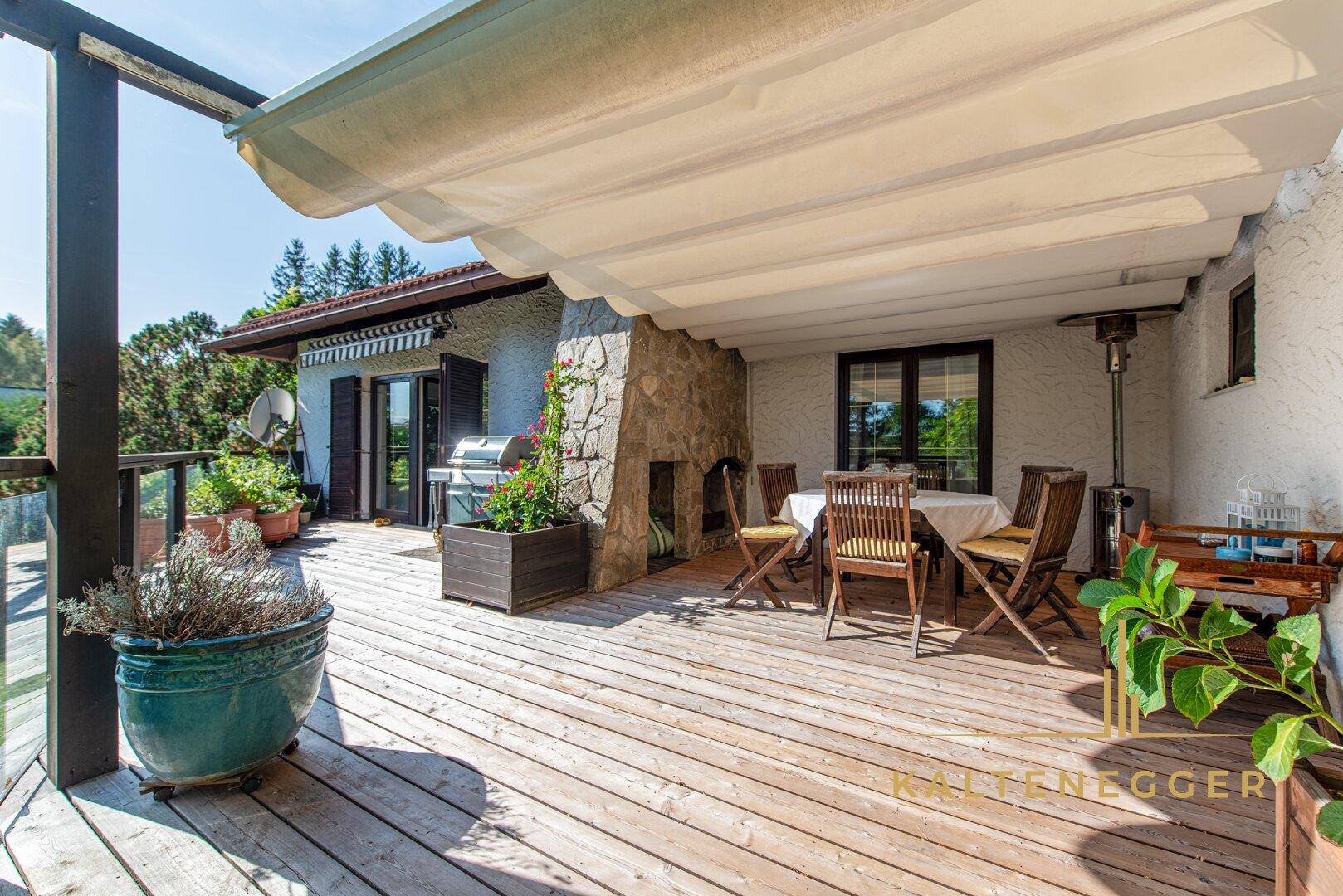 Gemütliche überdachte Holzterrasse mit Esstisch, Grillbereich und Pflanzen für entspannte Stunden im Freien.