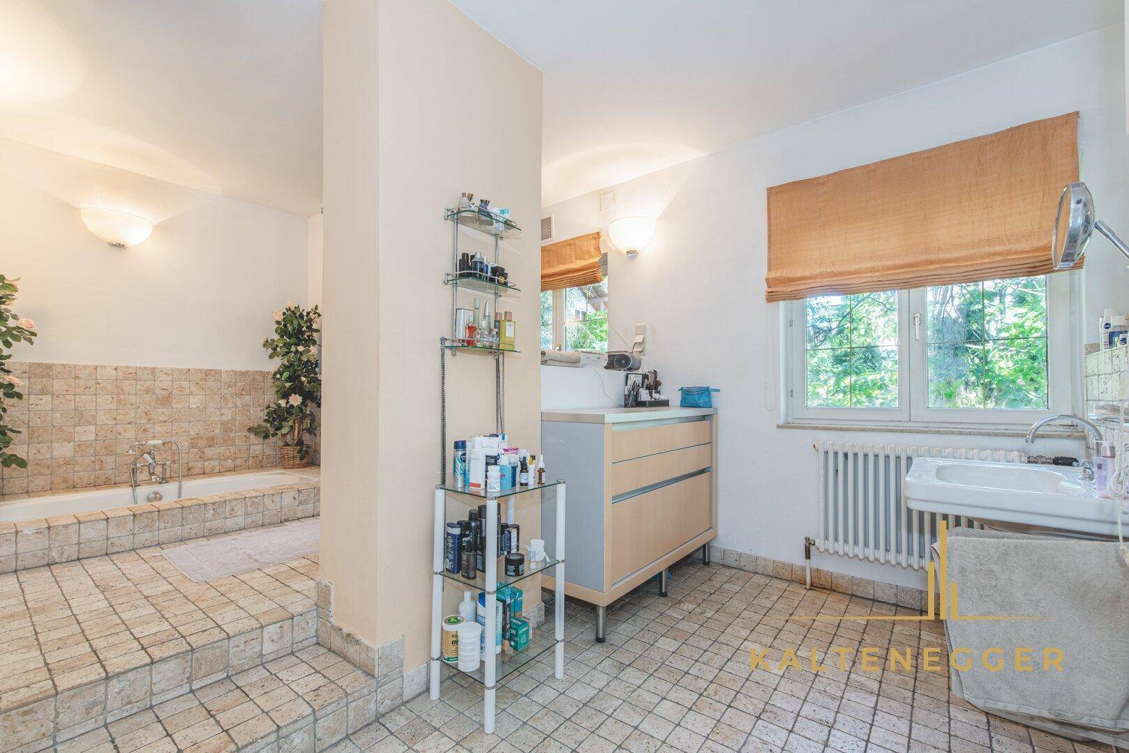 Geräumiges Badezimmer mit eingelassener Badewanne, Fenster und beigefarbenen Fliesen.