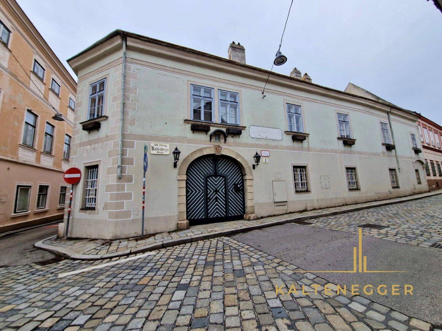 Detailansicht des historischen Gebäudes mit markantem Torbogen, Fensterläden und gepflasterter Straße.