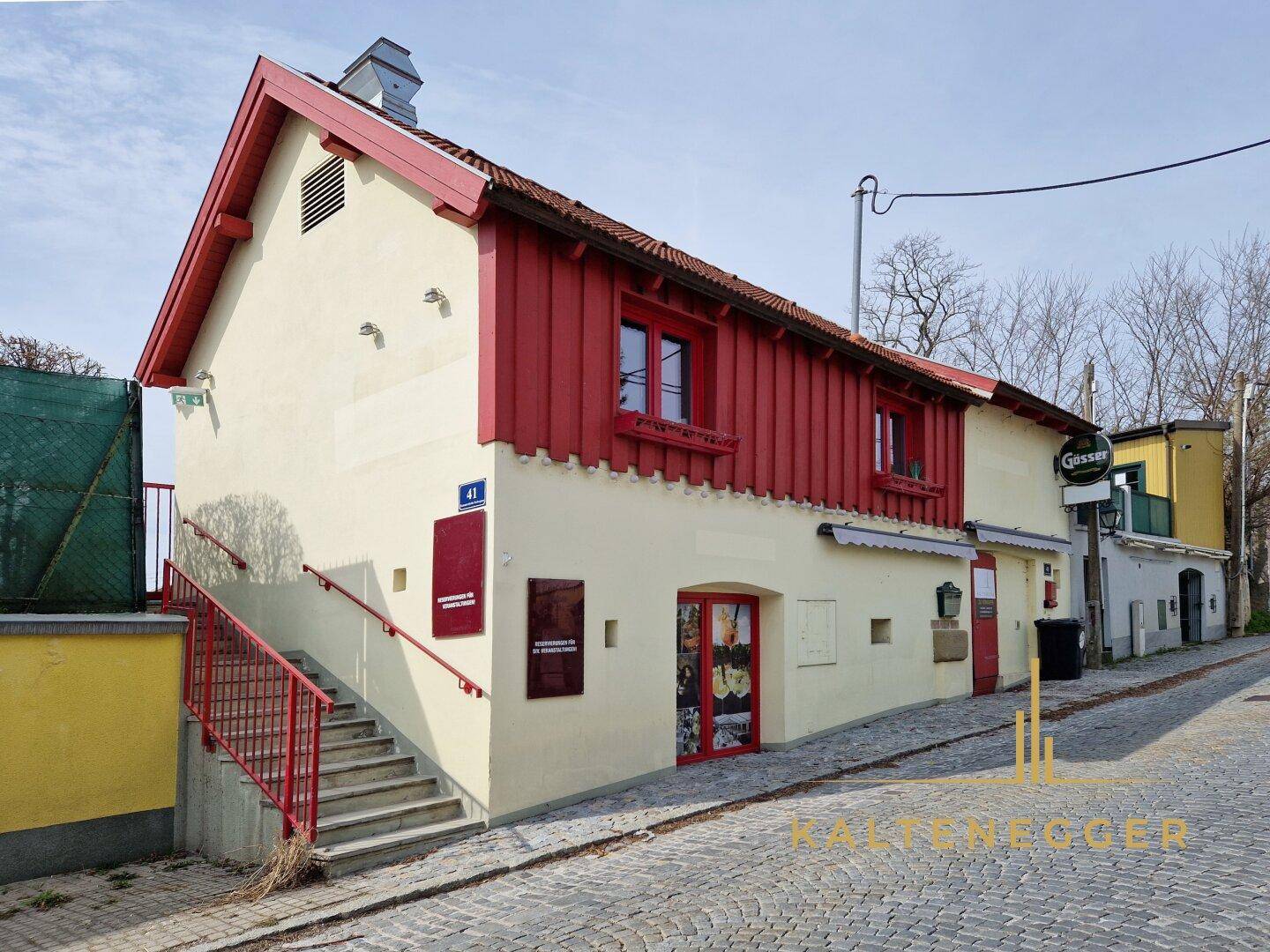 Traditionelles Gebäude mit roter Holzverkleidung und beiger Fassade an einer gepflasterten Straße.