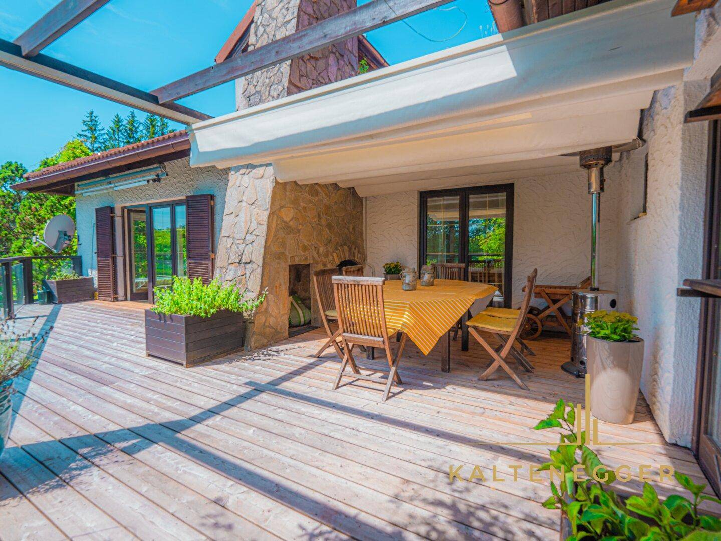 Sonnige Holzterrasse mit Essbereich und Steinkamin, perfekt für entspannte Stunden im Freien.