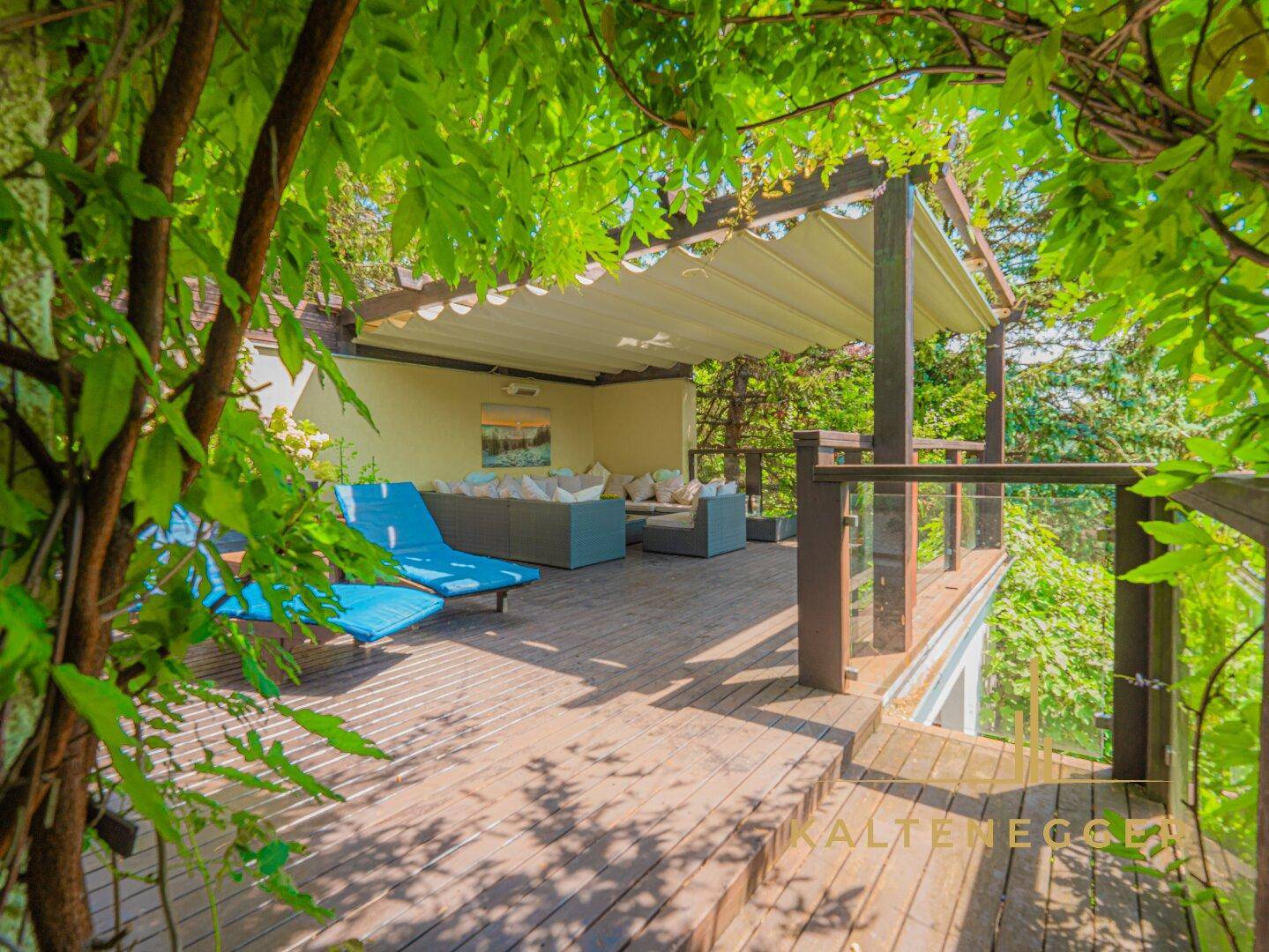 Idyllische Holzterrasse mit bequemen Lounge-Möbeln, Sonnenliegen und üppiger Begrünung.