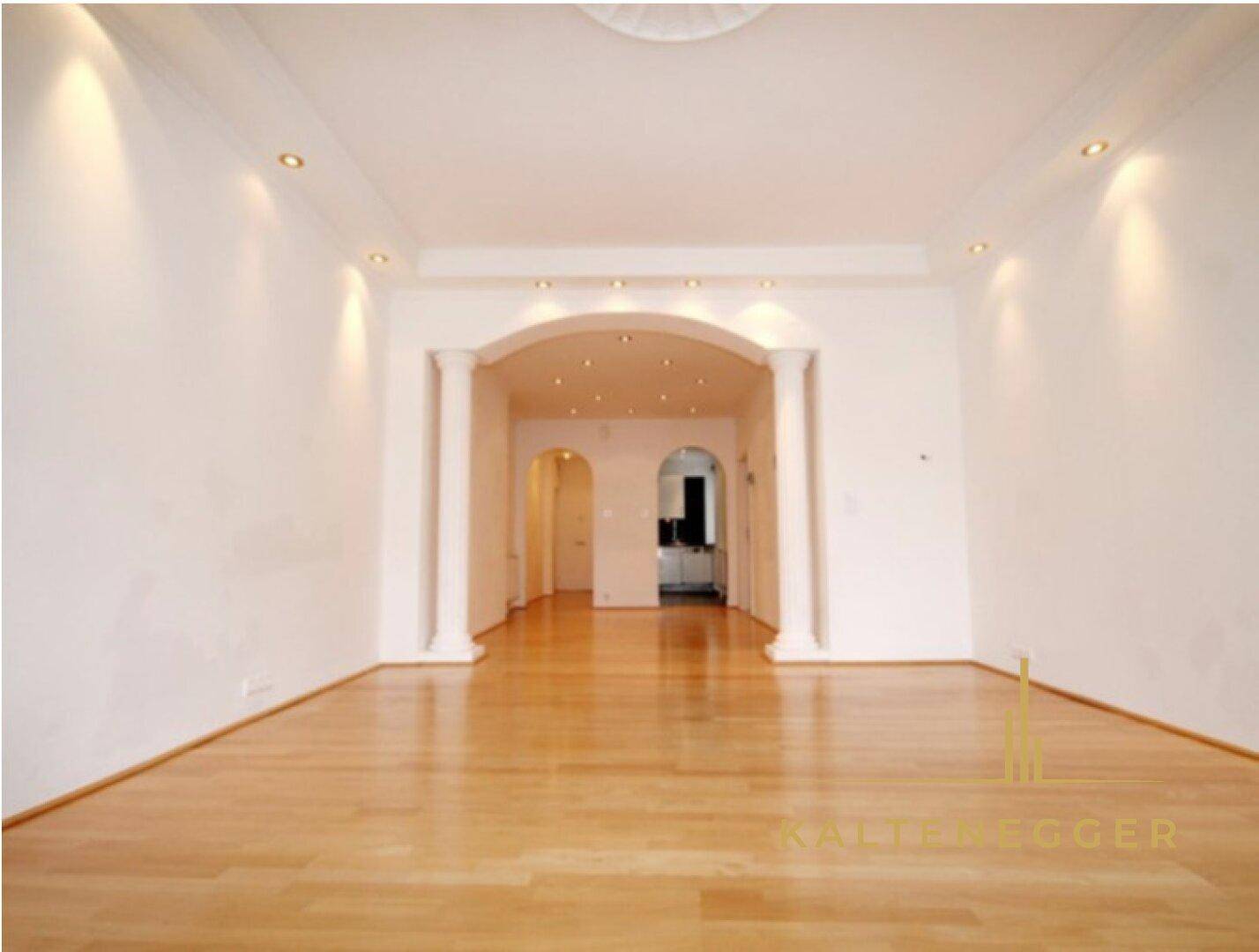 Heller Wohnraum mit Parkettboden, weißen Wänden und einem eleganten Bogendurchgang.