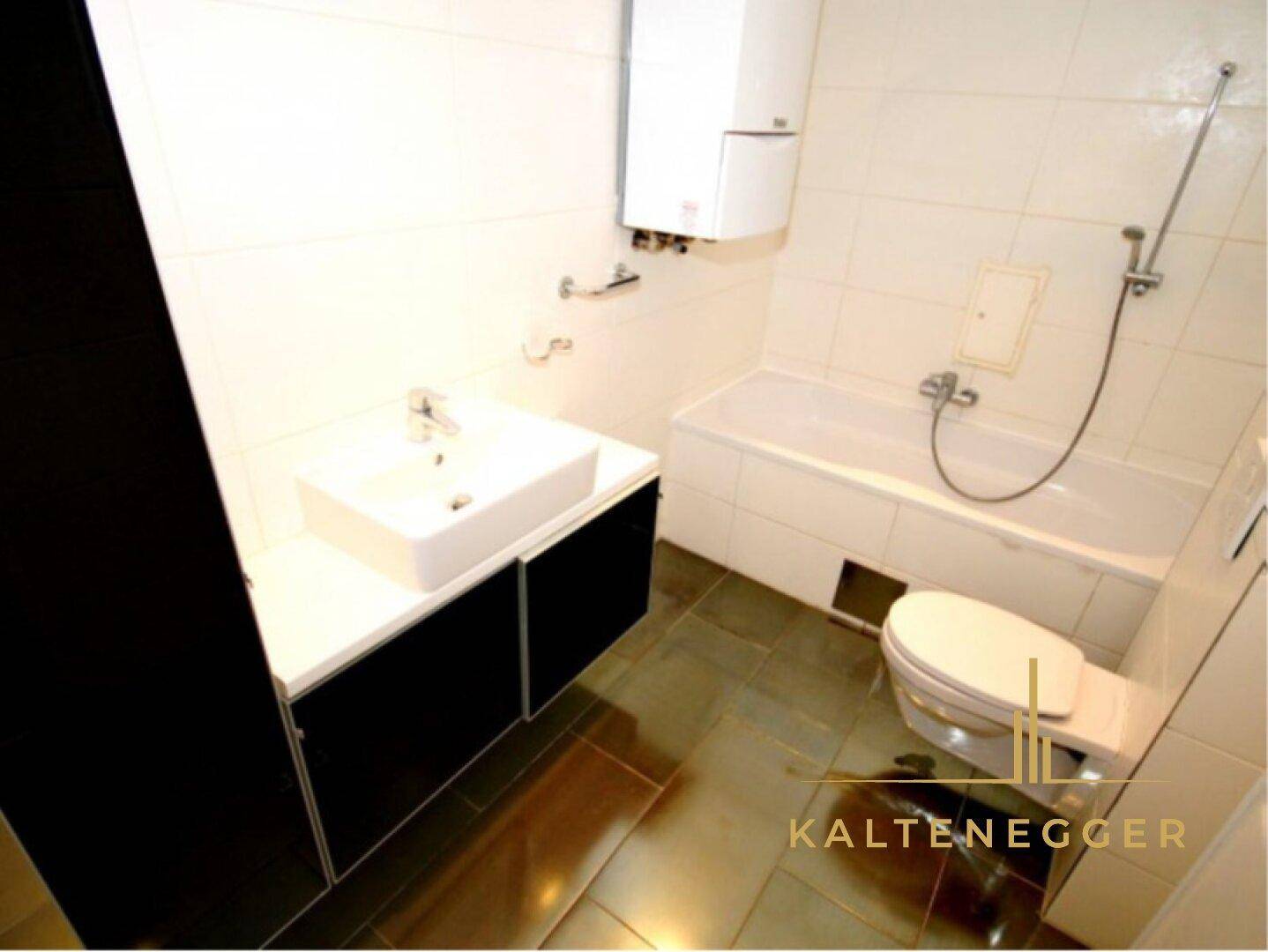 Funktionales Badezimmer mit Badewanne, Waschbecken und Toilette, komplett gefliest in Weiß.