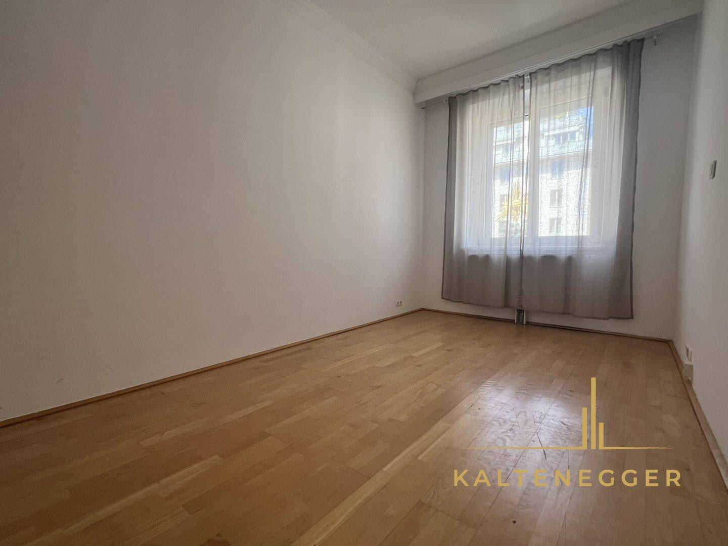 Schlichtes Zimmer mit Parkettboden und einem Fenster, das viel Tageslicht hereinlässt.