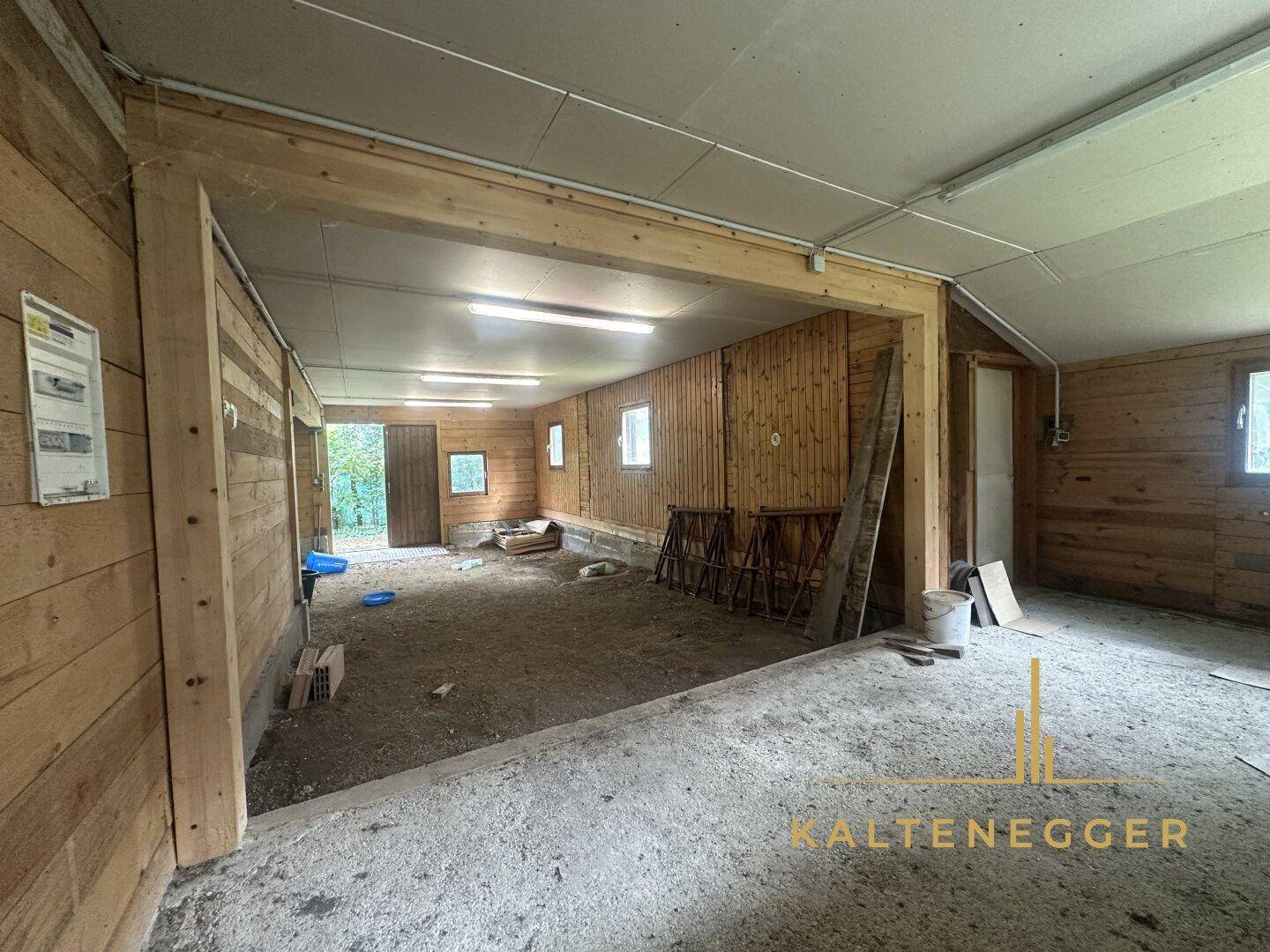 Innenansicht eines Holzgebäudes mit Betonboden im Vordergrund und Holzwänden.