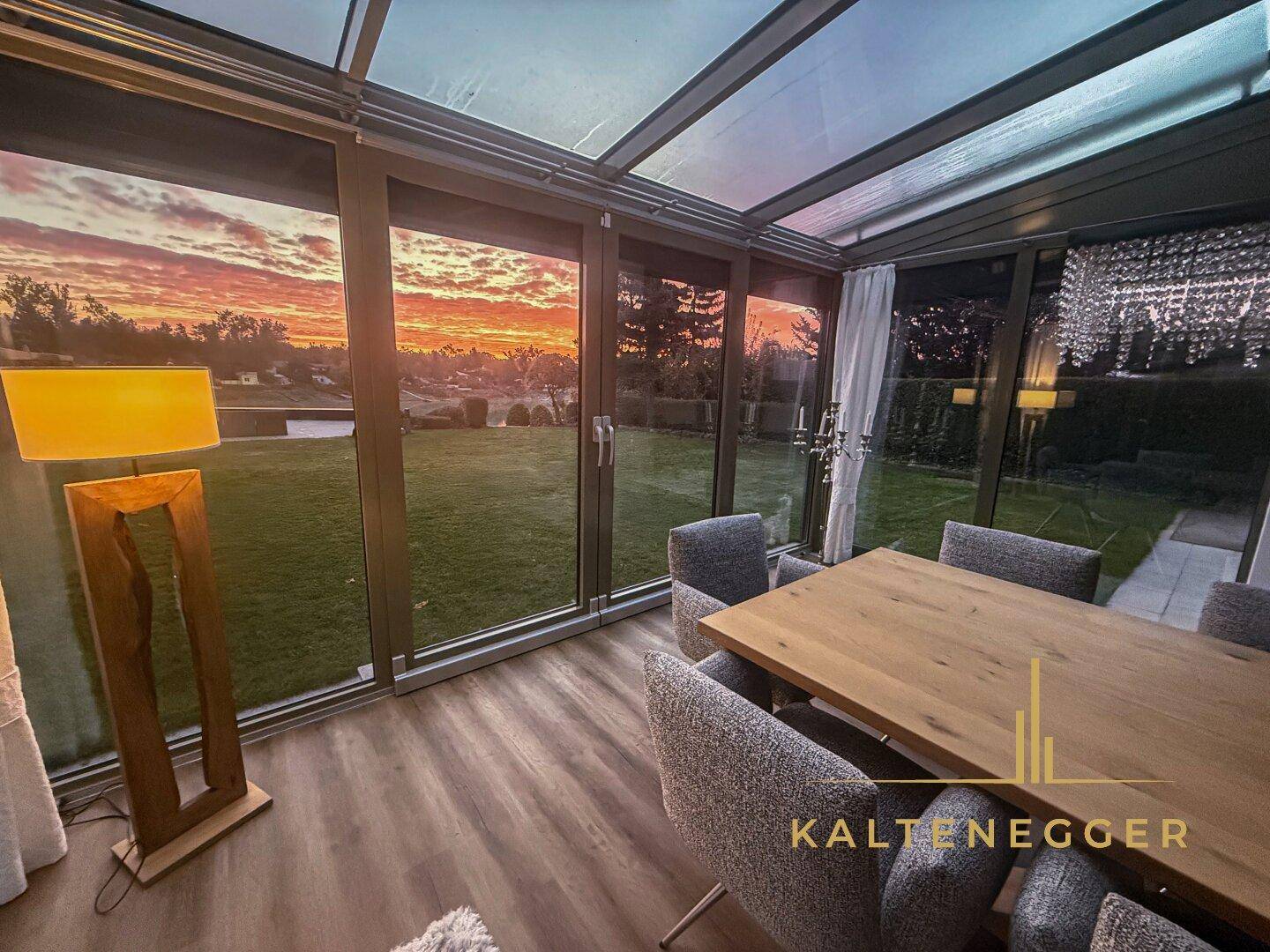 Essbereich im Wintergarten mit Panoramablick auf den Sonnenuntergang und den Garten.