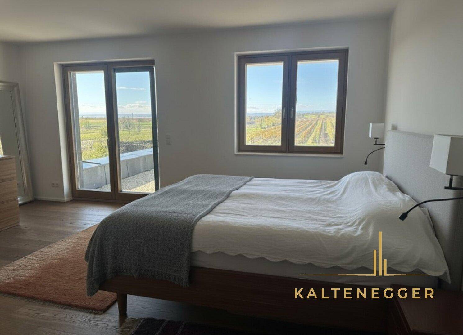 Helles Schlafzimmer mit Holzboden, großen Fenstern und Blick auf die umliegende Landschaft.