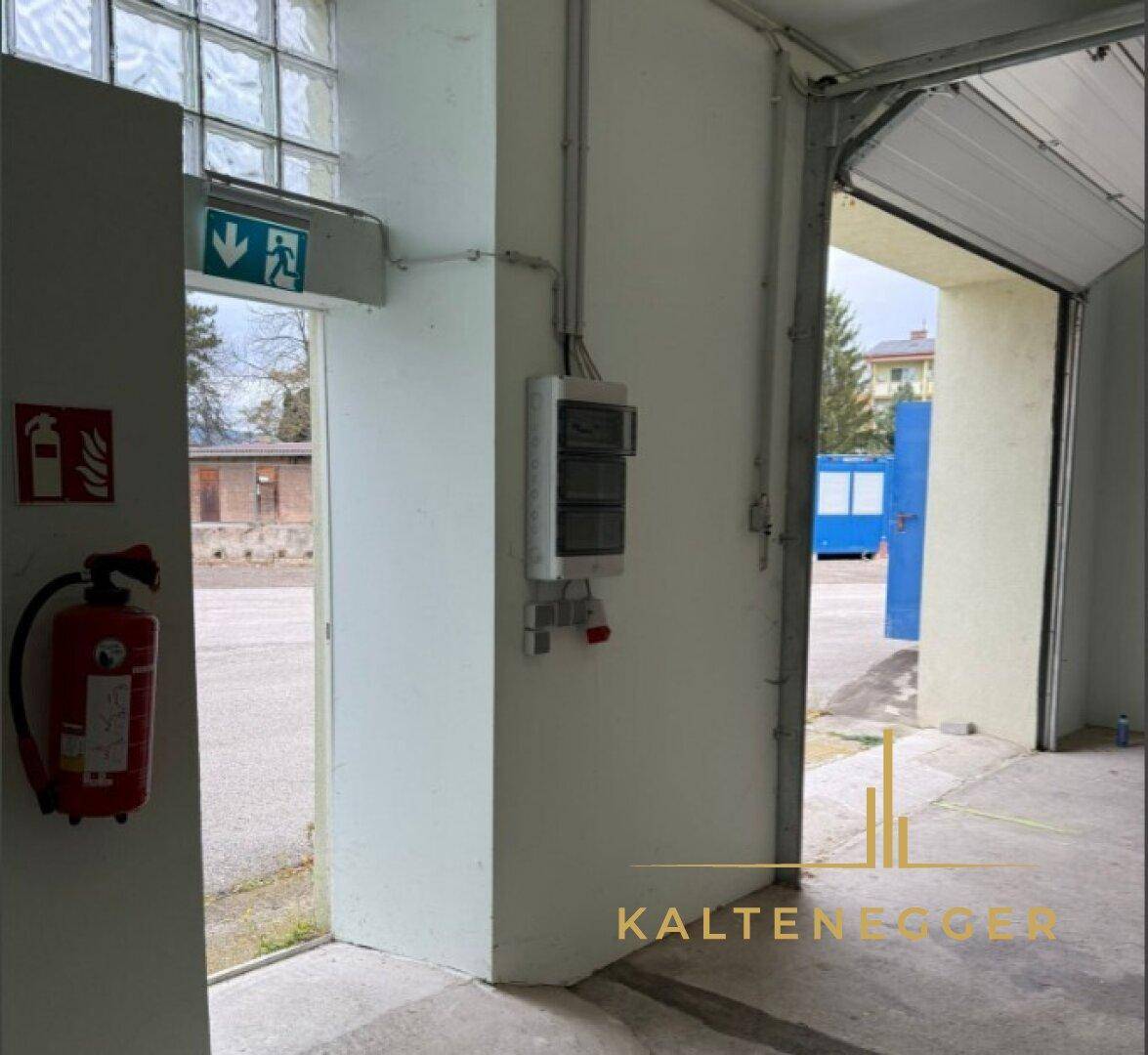 Funktionaler Bereich mit Notausgang, Feuerlöscher und elektrischem Schaltkasten, gut beleuchtet.