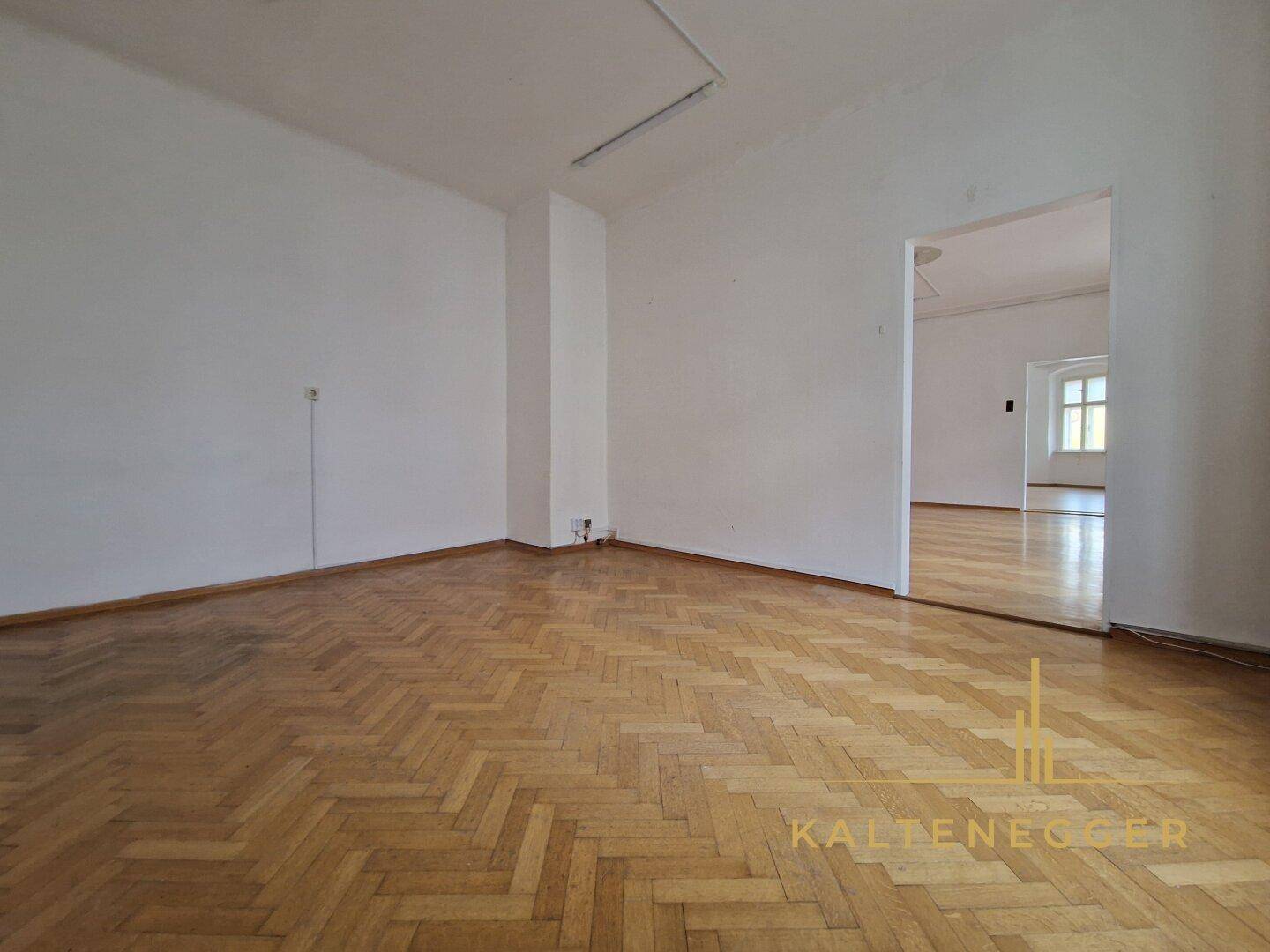Geräumiger Raum mit klassischem Fischgrätparkett und hohen Decken, ideal für einen Wohnbereich.