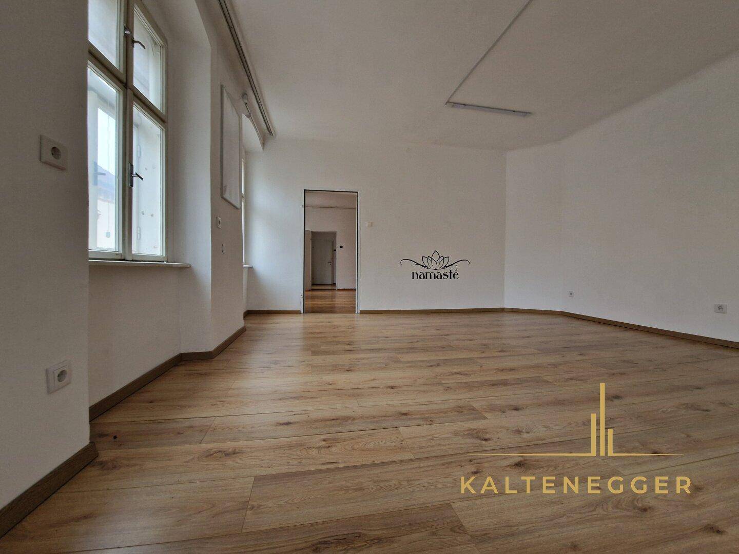 Lichtdurchfluteter Raum mit Laminatboden und großen Fenstern, geeignet für Wohn- oder Arbeitszwecke.