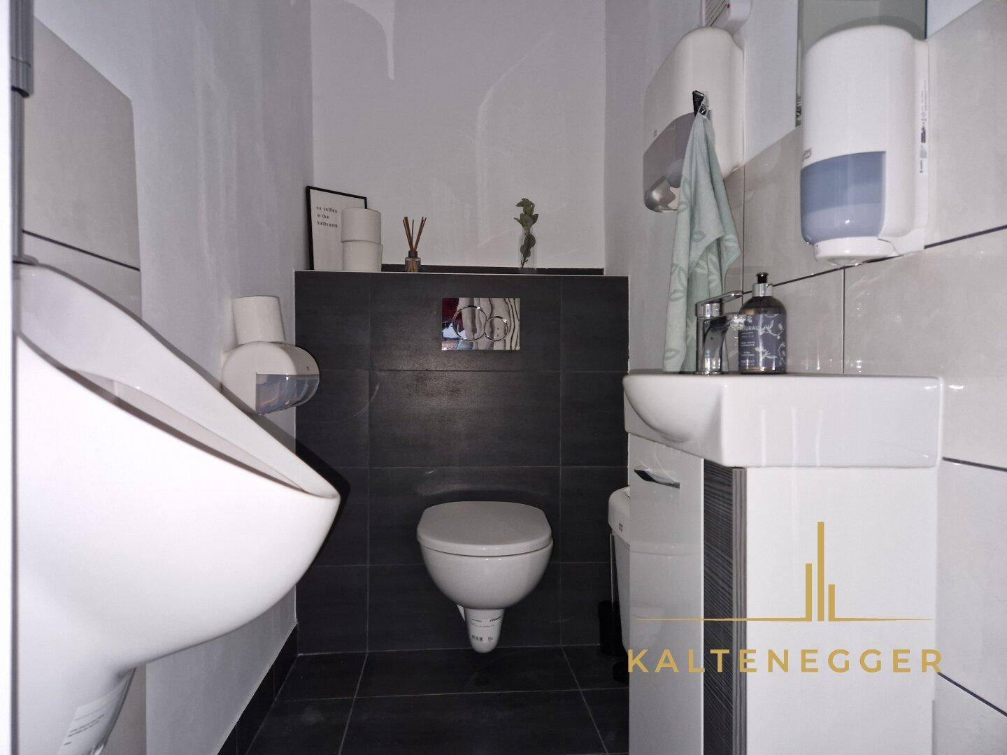 Modern geflieste Gästetoilette mit zwei Waschbecken und Wand-WC in dunklen und hellen Tönen.