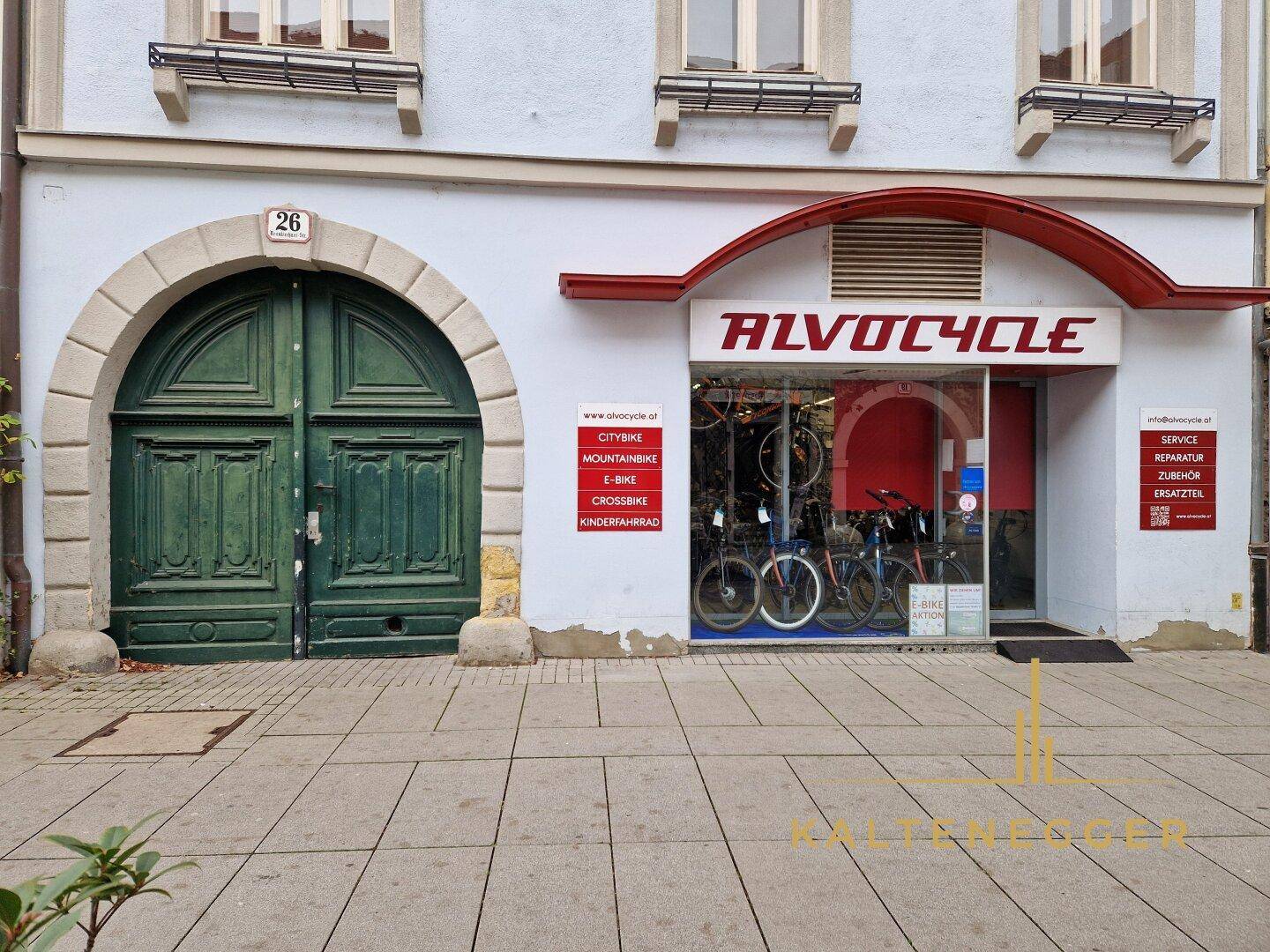 Historische Fassade mit einem großen Holztor und einem Fahrradgeschäft im Erdgeschoss.