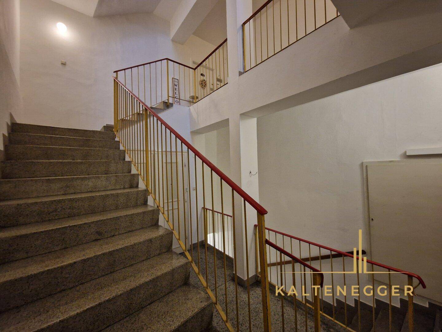 Geräumiges Treppenhaus mit Steinstufen und gelb-rotem Geländer in einem Altbau.